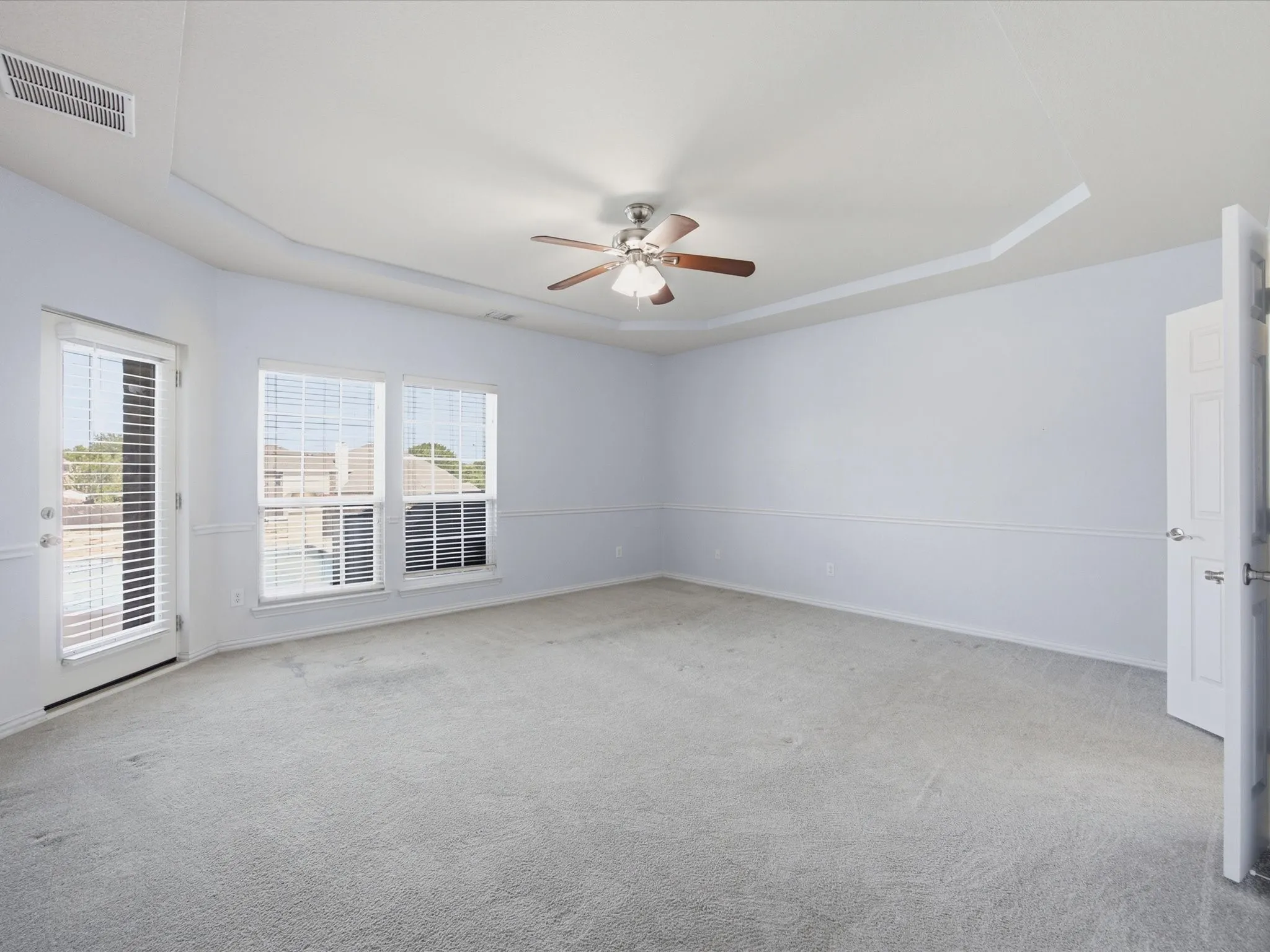Spacious interior featuring neutral carpeting, ceiling fan with integrated lighting, and abundant natural light from multiple glass doors and windows