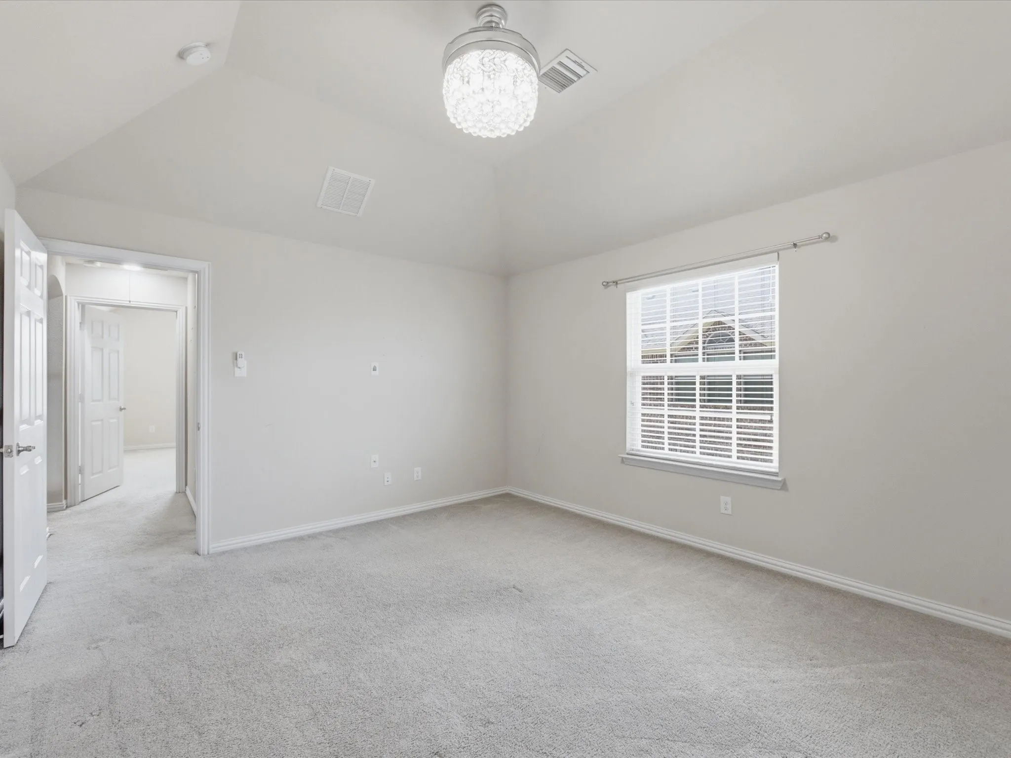 Vaulted ceiling with a decorative light fixture, neutral carpet, and a window with blinds