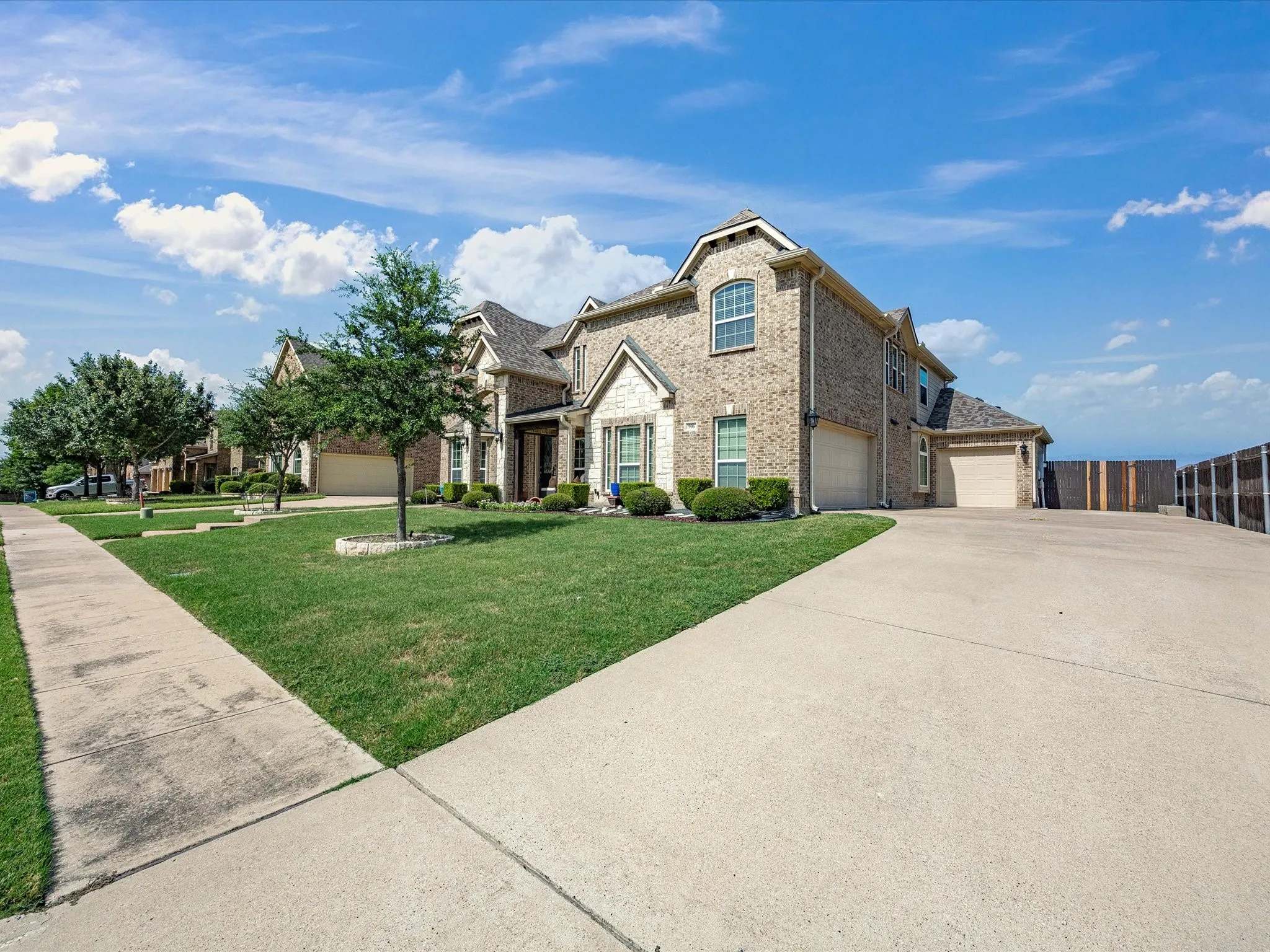 Brick and stone facade, dormer windows, attached garage, concrete driveway, and manicured landscaping