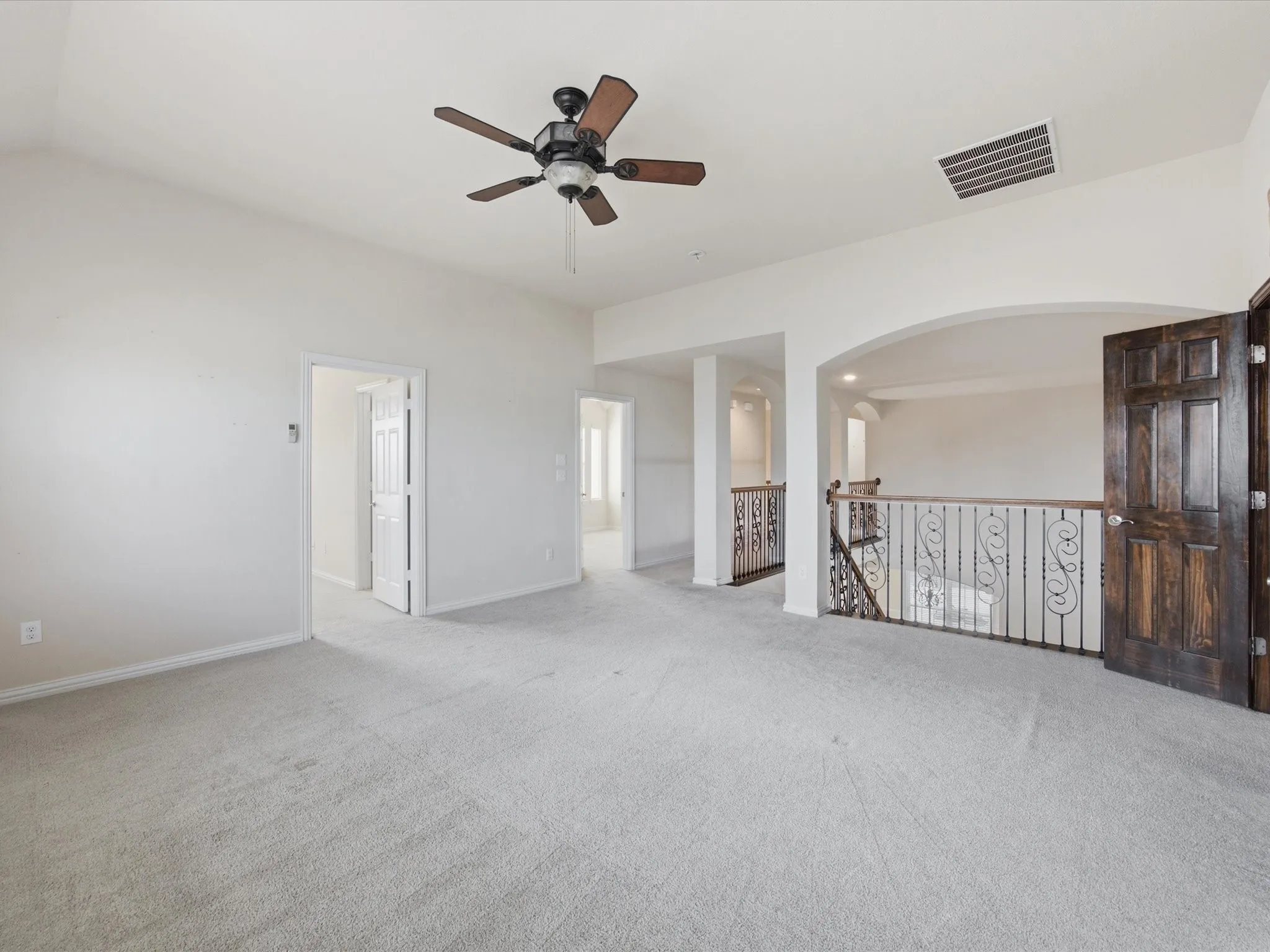 Expansive carpeted area featuring a ceiling fan, a vaulted ceiling, and an arched entryway