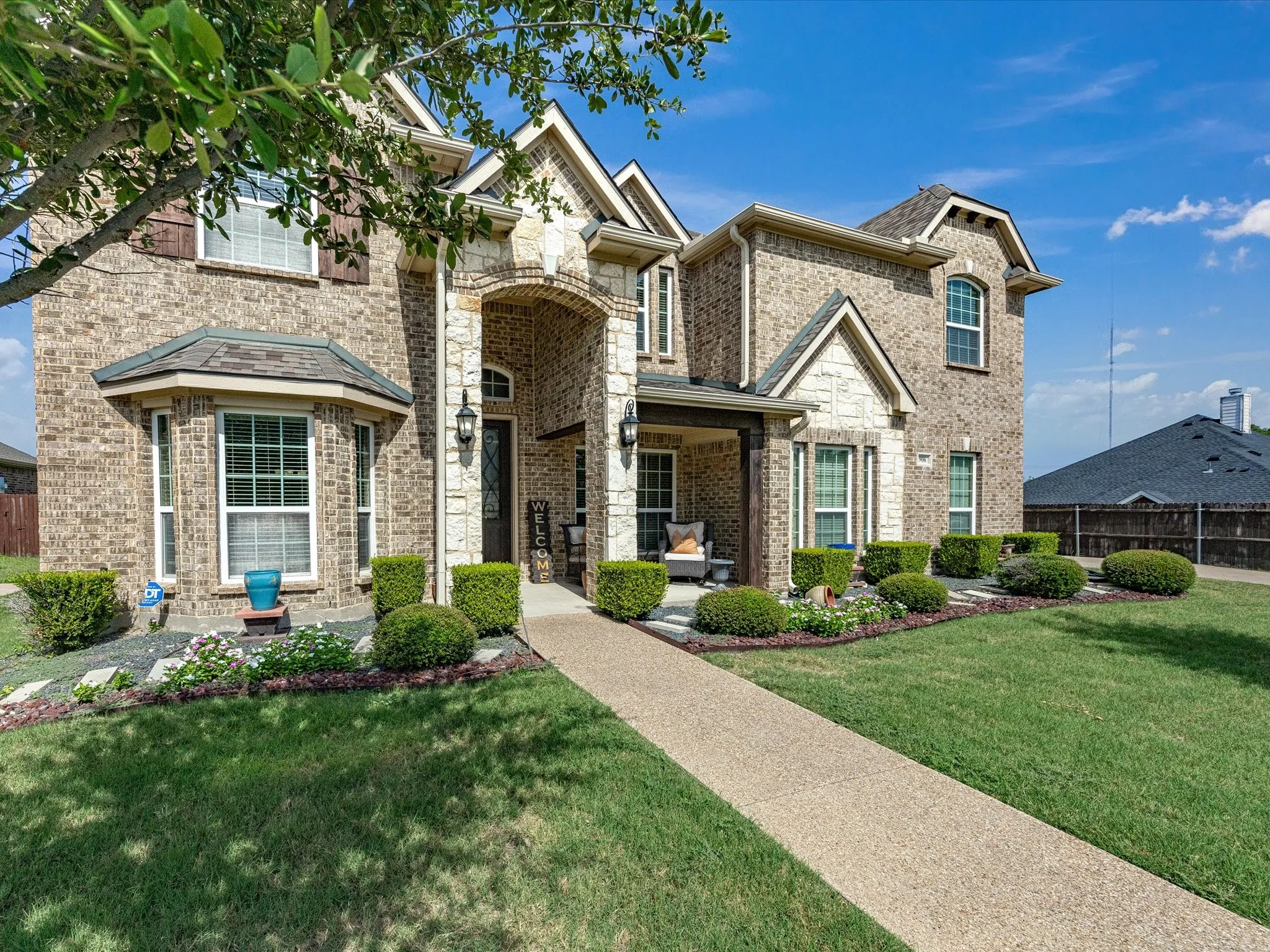 Brick and stone facade, covered porch entry, bay window, landscaped front yard, and an exposed aggregate walkway