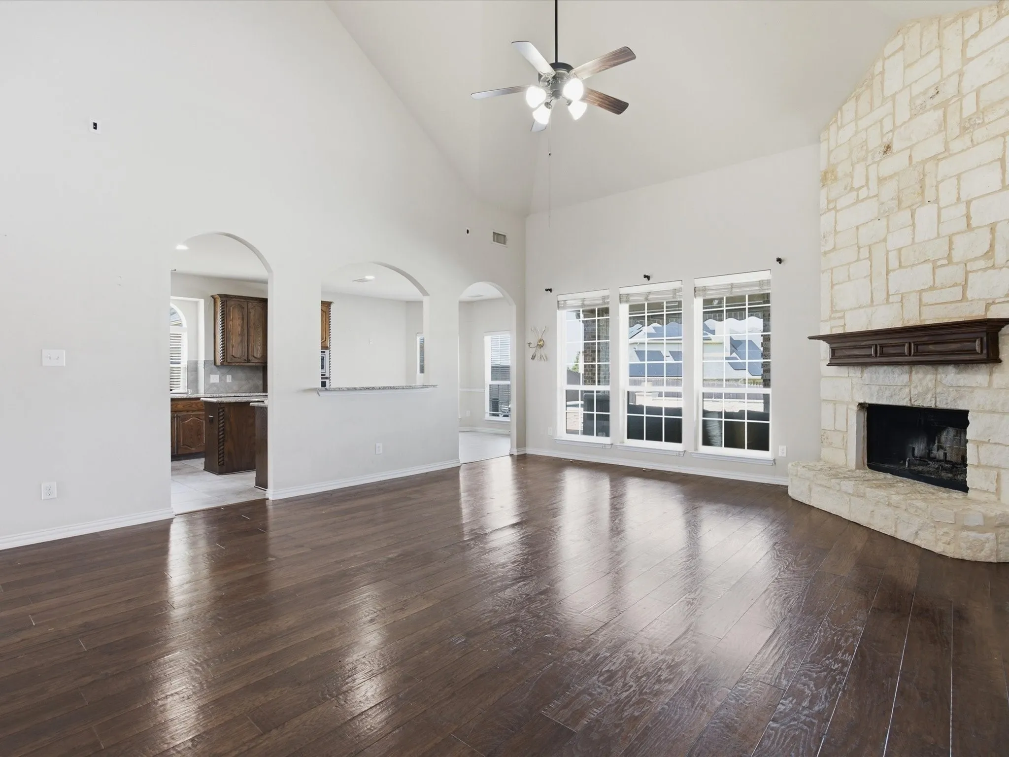 Vaulted ceilings with a ceiling fan, stone-clad fireplace with a decorative mantel, wood-finish flooring, and arched doorways