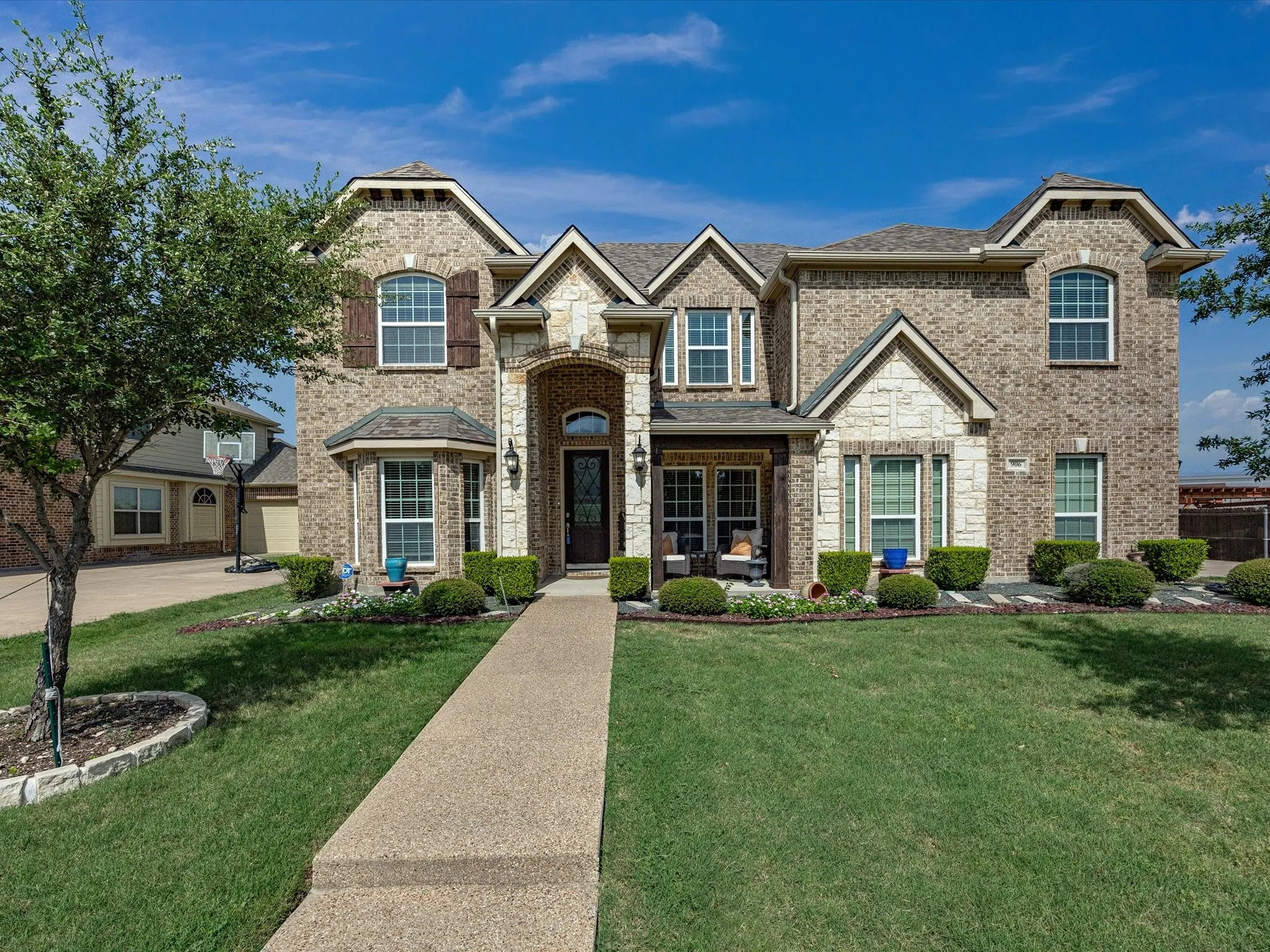Brick and stone facade with multiple gables, covered entry porch, bay window, and manicured landscaping