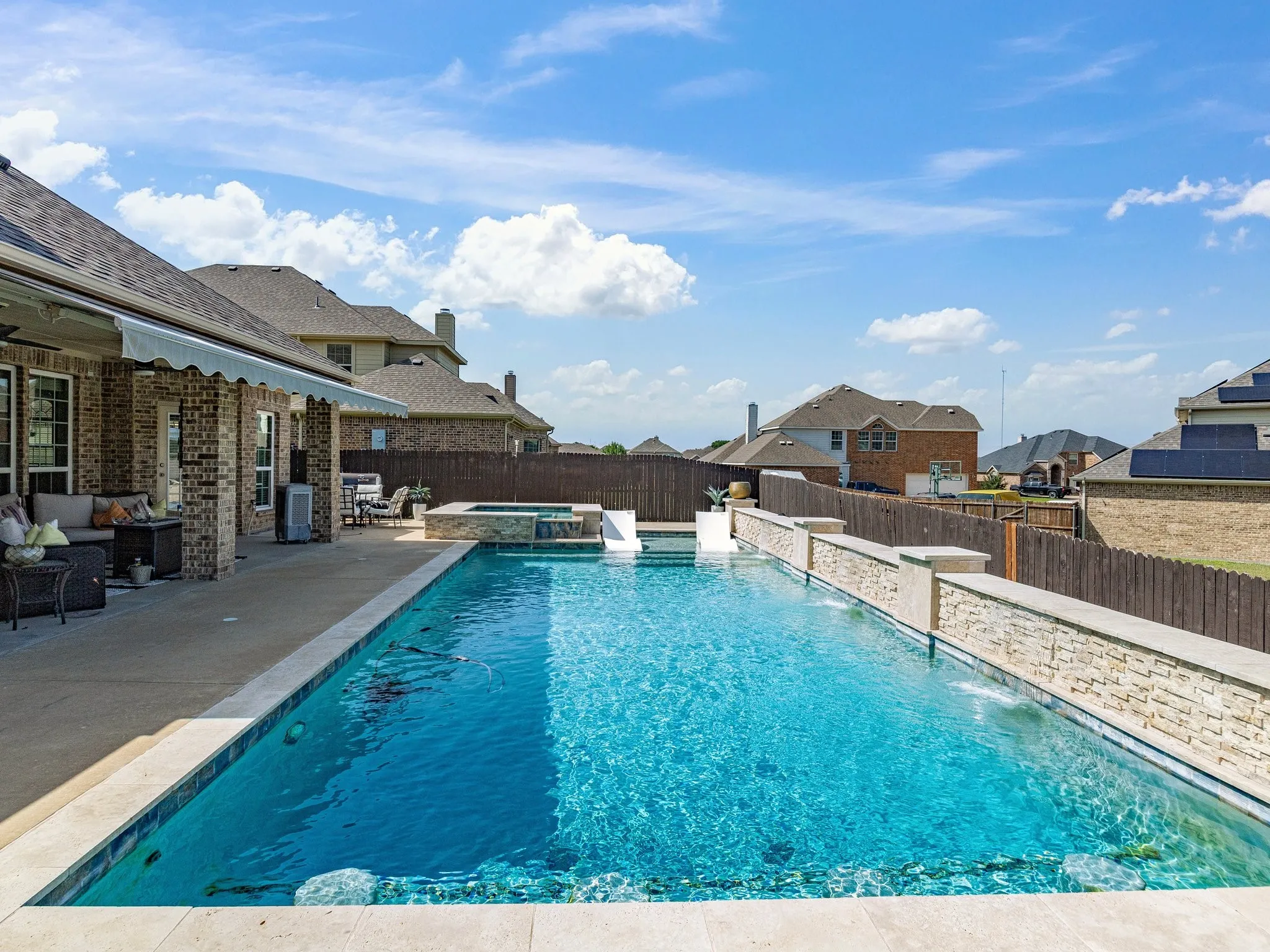 Expansive outdoor living area featuring a rectangular swimming pool, integrated spa, and a covered patio with a retractable awning