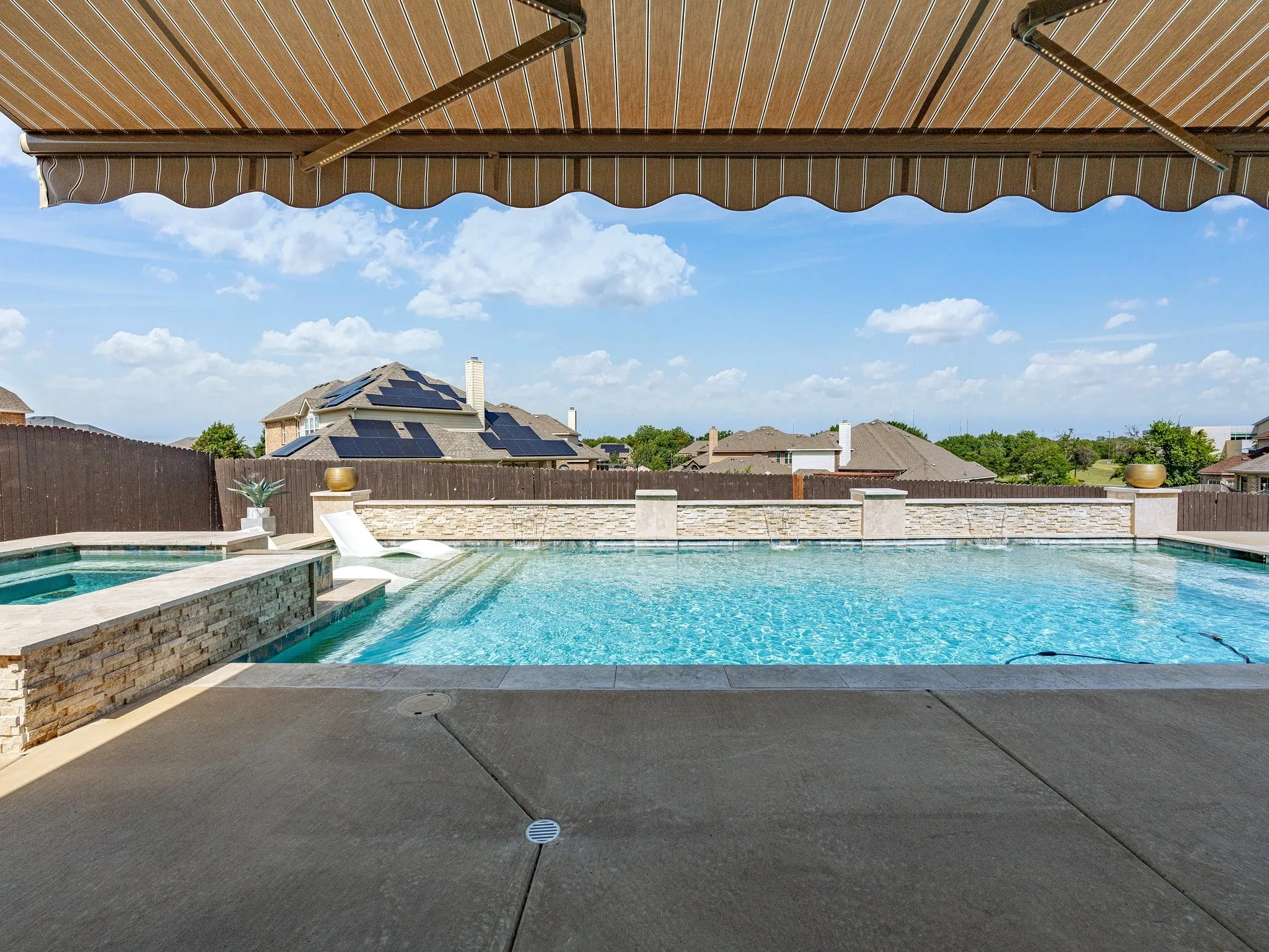 Outdoor swimming pool with an integrated spa, surrounded by concrete decking and a stone-clad retaining wall