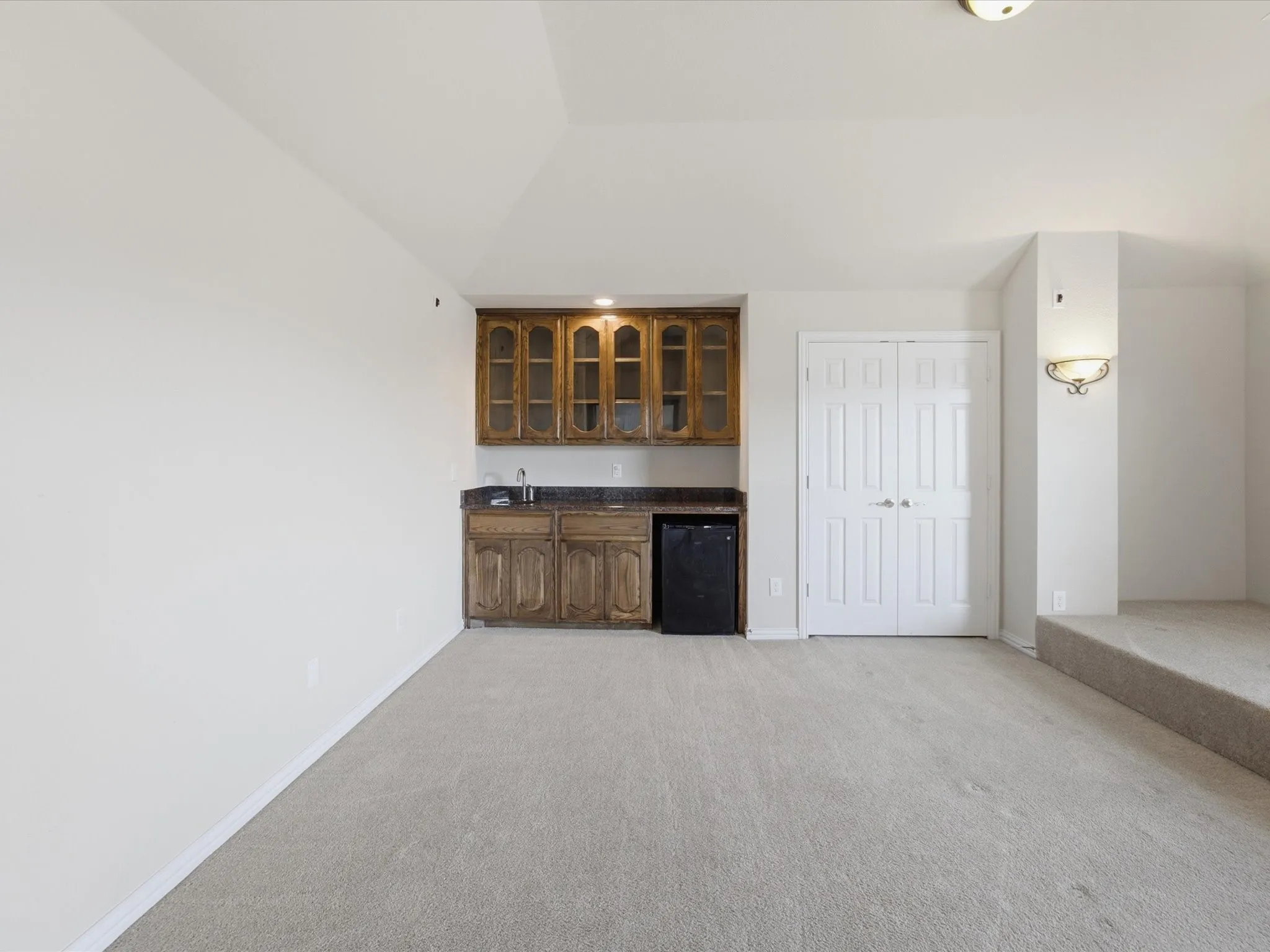 Built-in wet bar with wood cabinetry and dark countertop, integrated mini-refrigerator, and wall sconce lighting