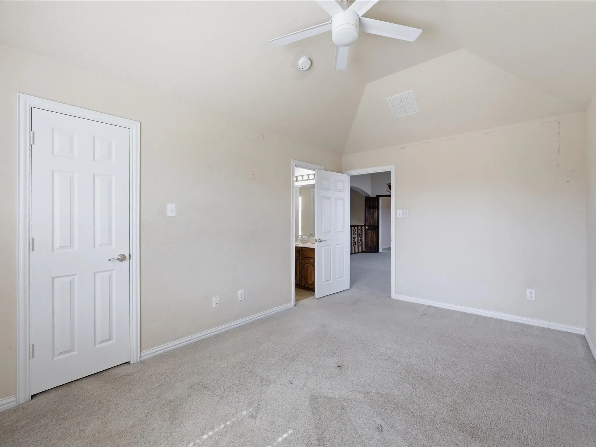 Spacious primary suite featuring vaulted ceilings, ceiling fan, neutral carpeting, and abundant natural light