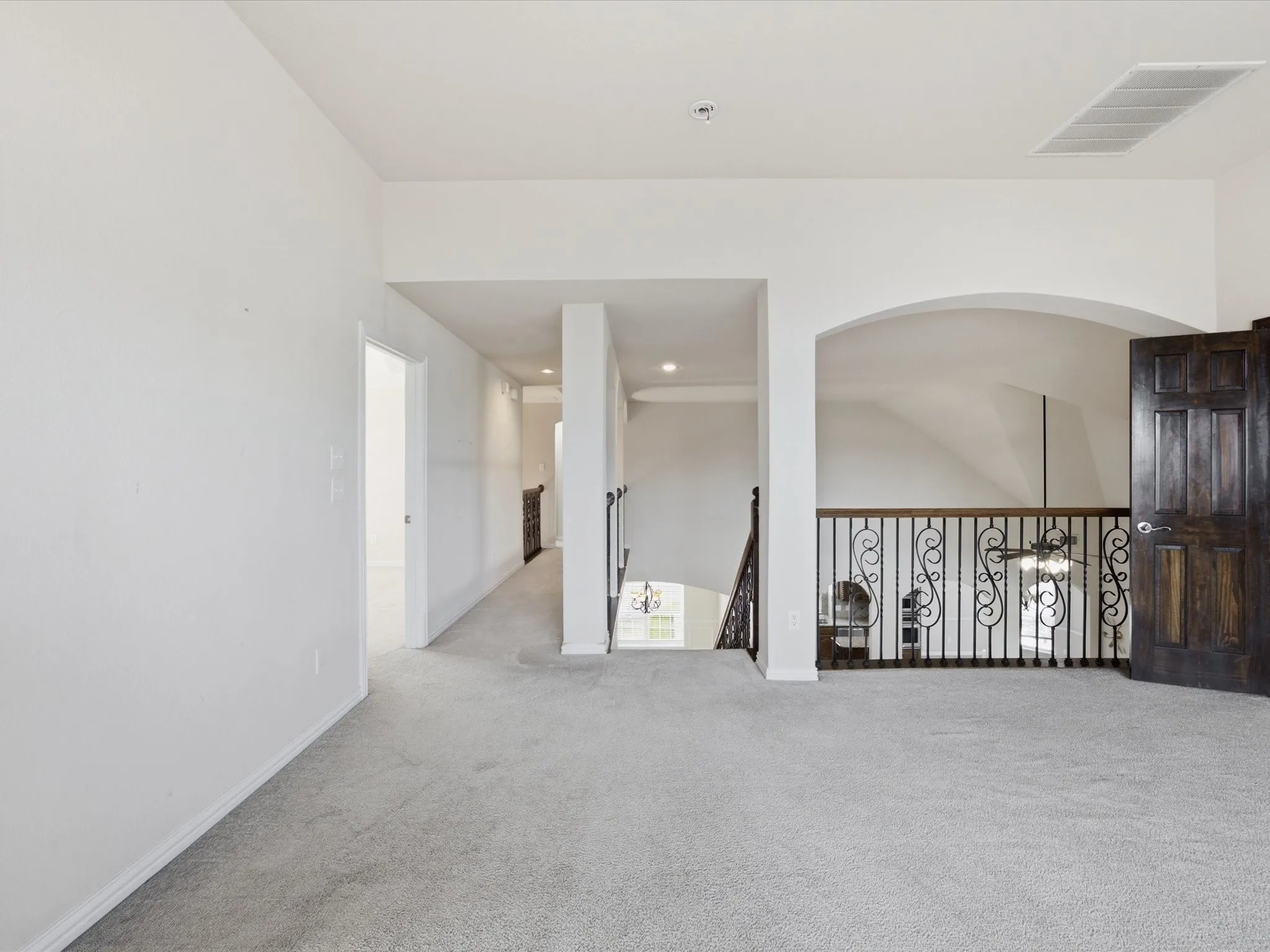 Carpeted flooring, white walls, dark wood-finish door, and wrought iron railing with decorative scrollwork
