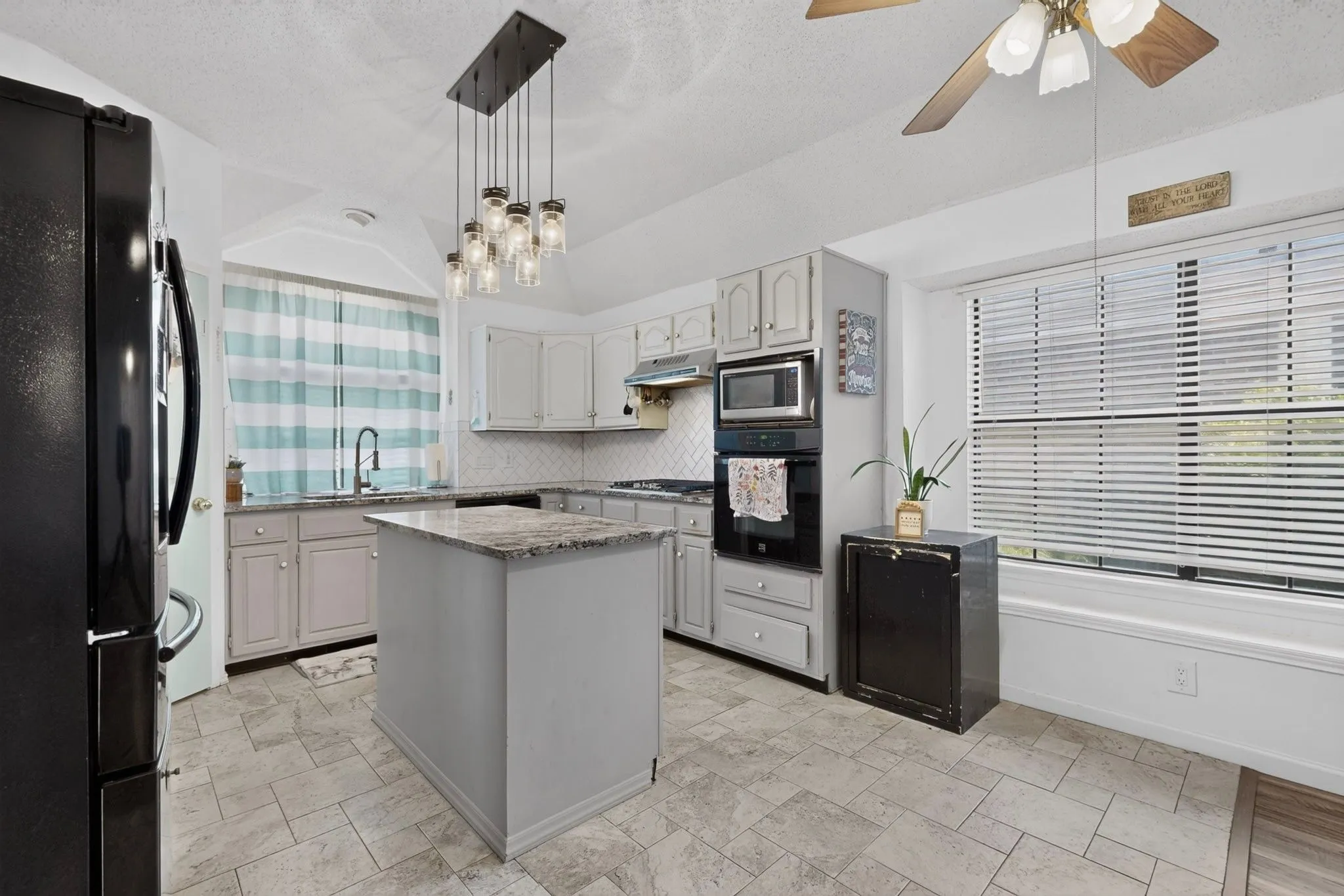 Kitchen featuring a center island with a stone countertop, light-toned cabinetry, built-in appliances, a tiled backsplash, and tiled flooring