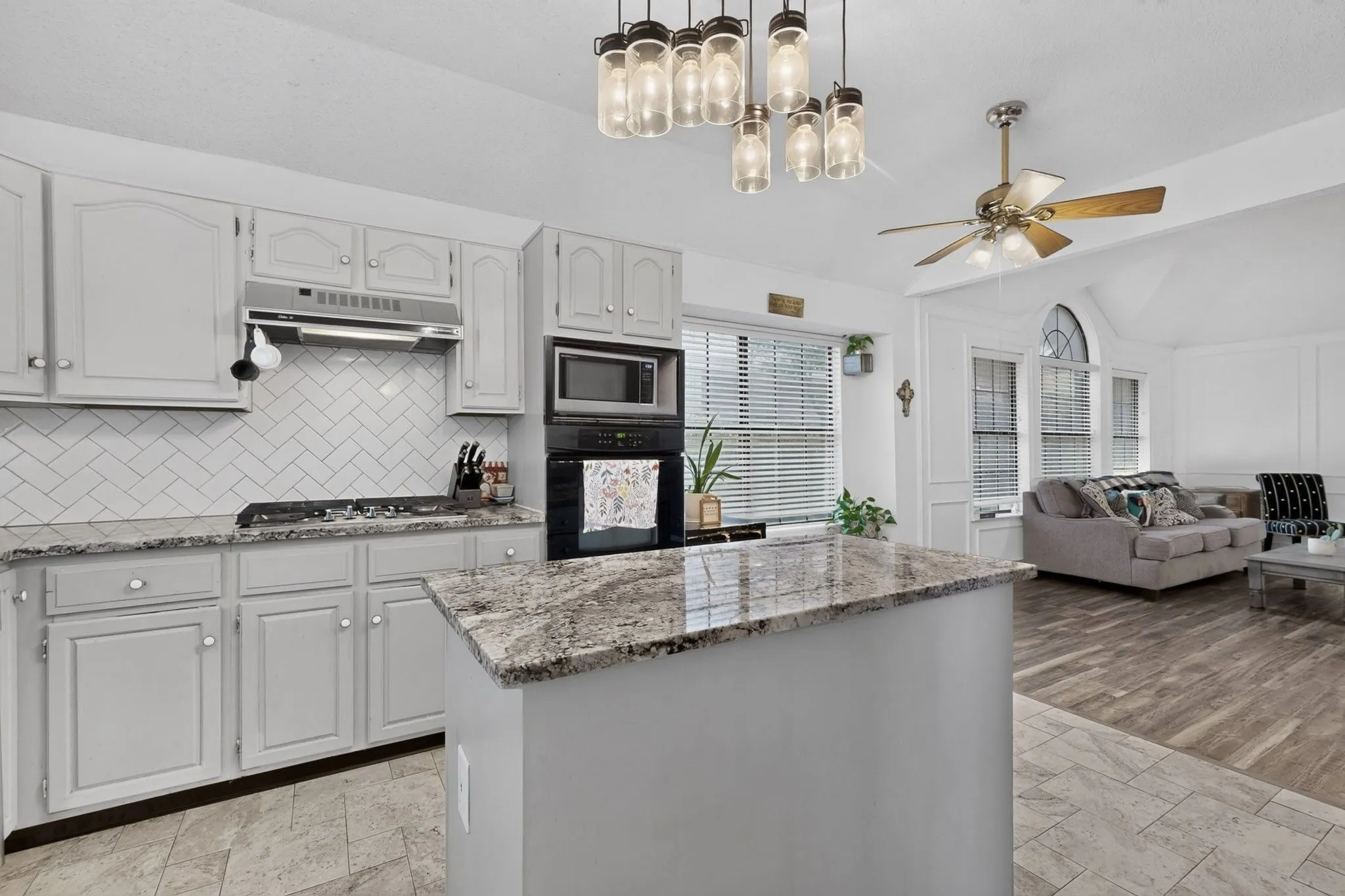 Kitchen featuring a central island with a granite countertop, light gray cabinetry, and a white herringbone tile backsplash