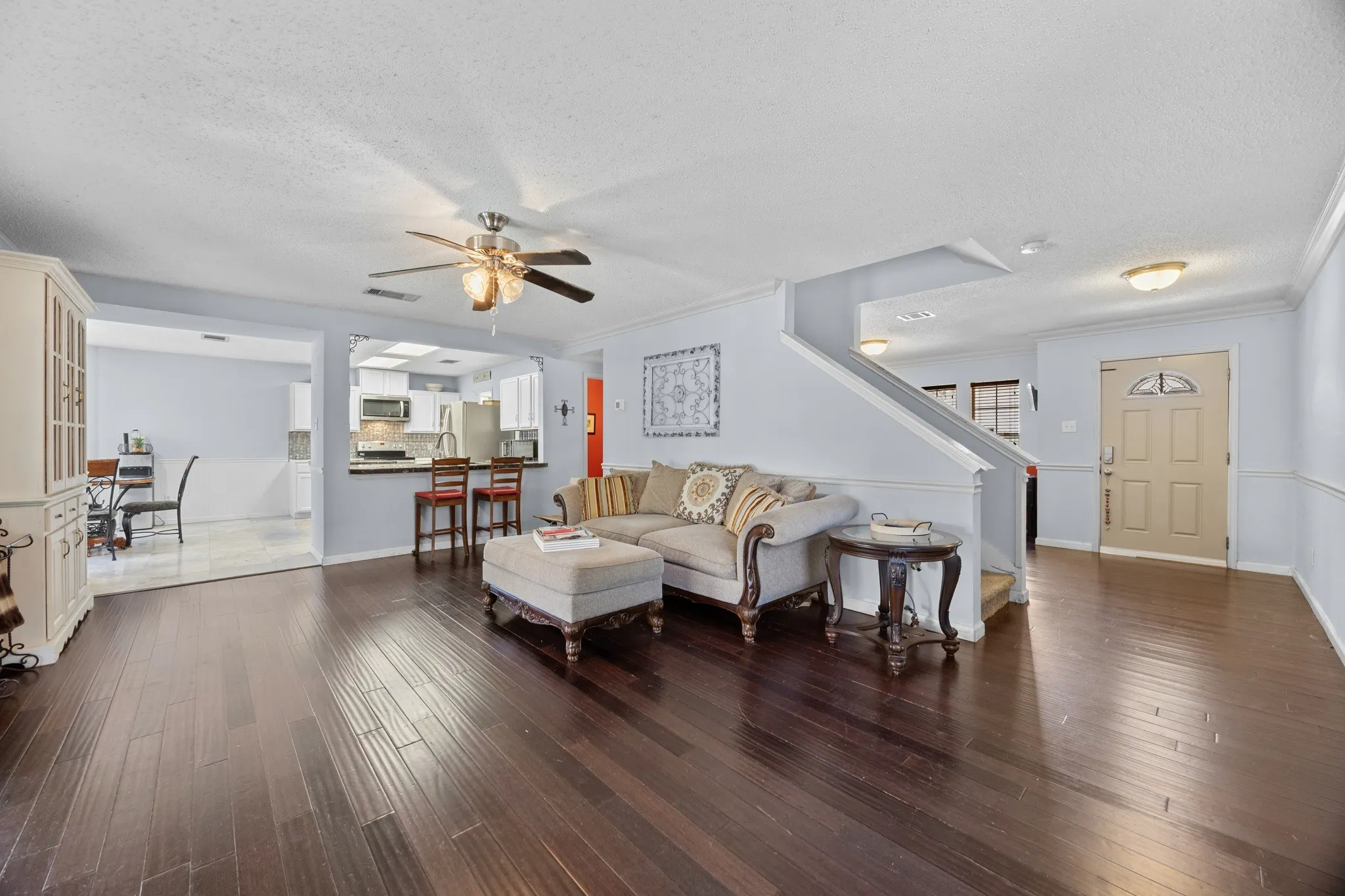 Open-concept living area featuring dark wood-finish flooring throughout, ceiling fan with integrated lighting, and abundant natural light
