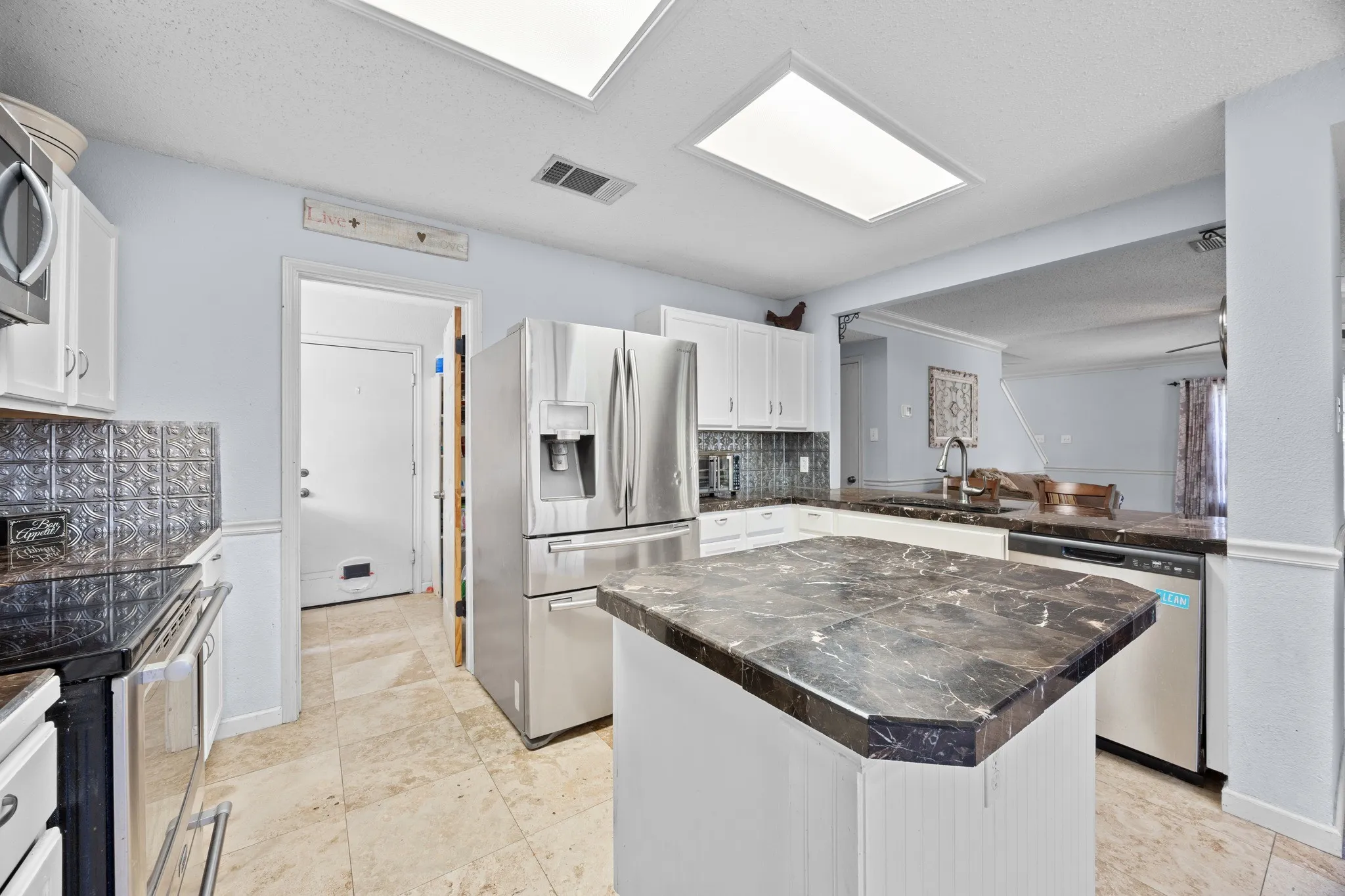 Kitchen featuring an island with a stone-finish countertop, white cabinetry, tile flooring, stainless steel appliances, and recessed lighting