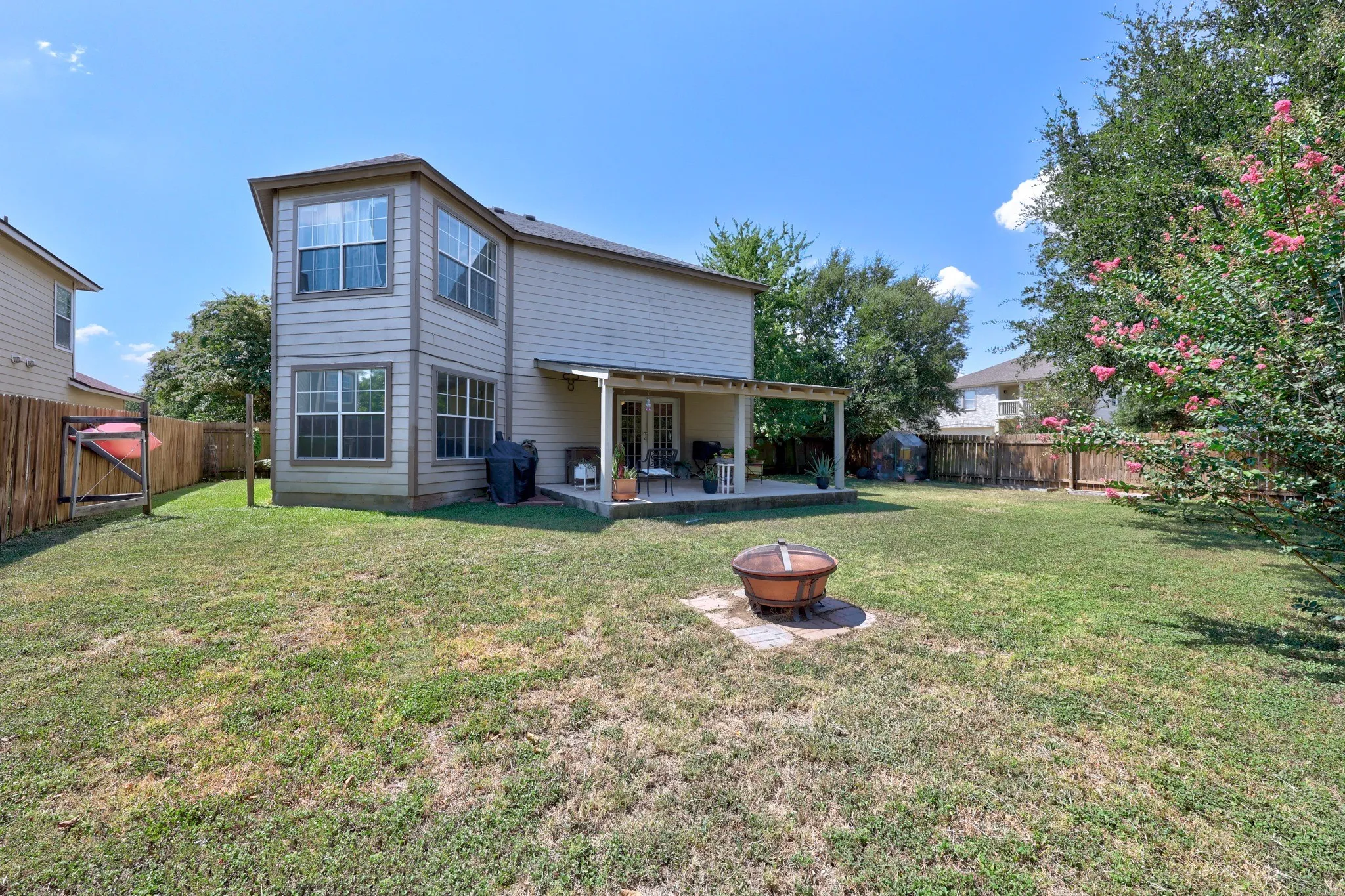 Two-story exterior with neutral siding, a covered patio, double-pane windows, and a fully fenced backyard