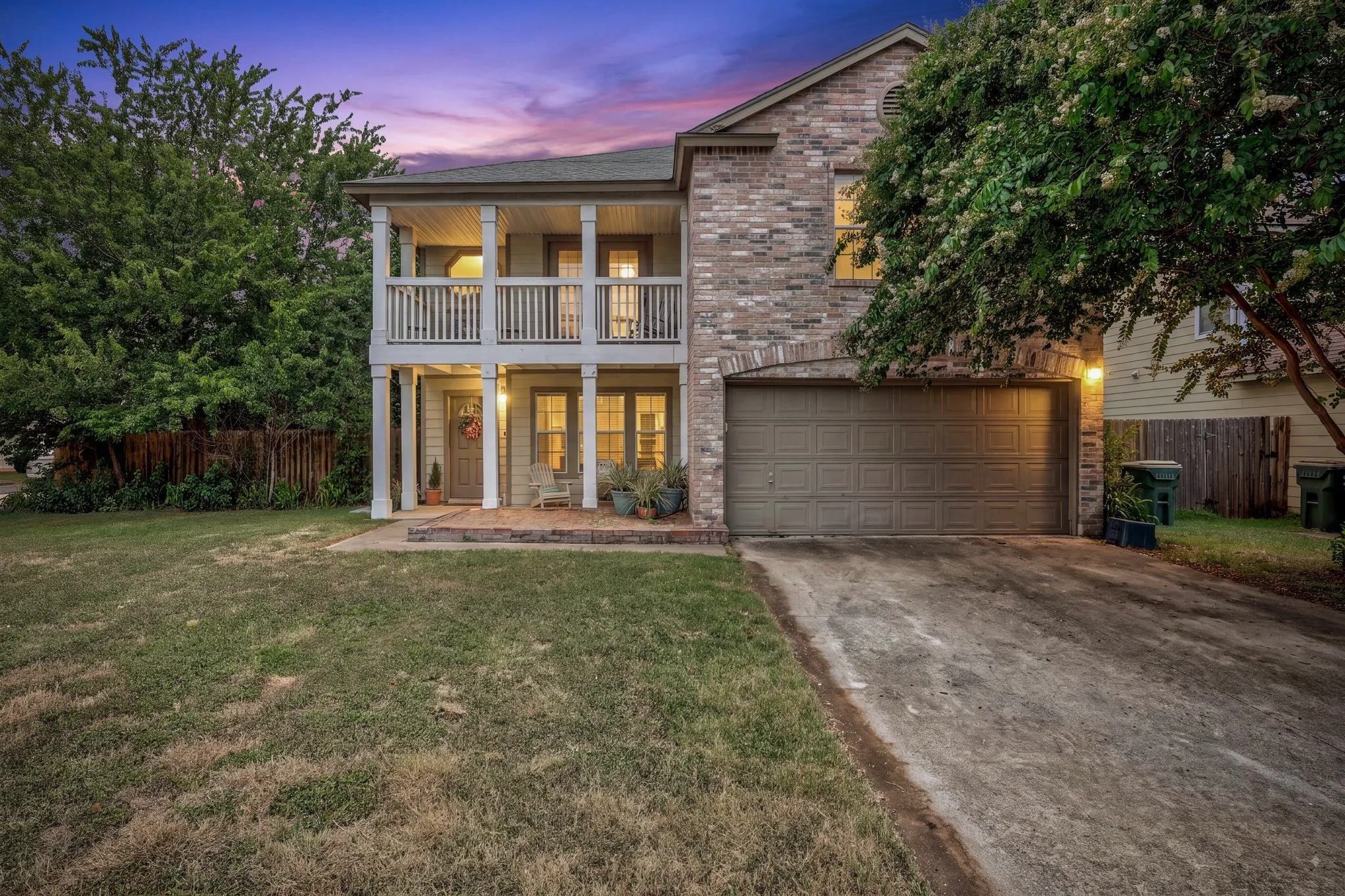 Brick facade, two-story porch, attached garage, concrete driveway, and mature landscaping