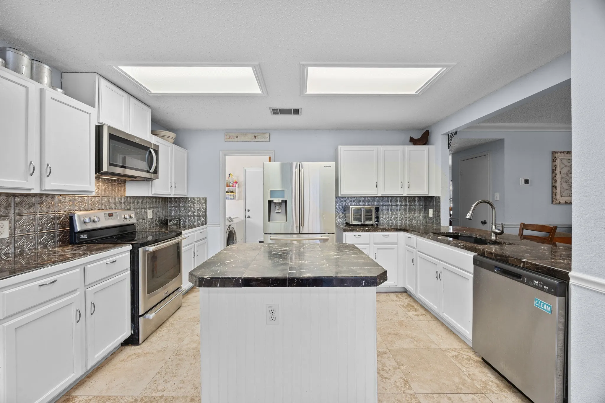 White cabinetry with stainless steel appliances, dark countertops, and a decorative tile backsplash