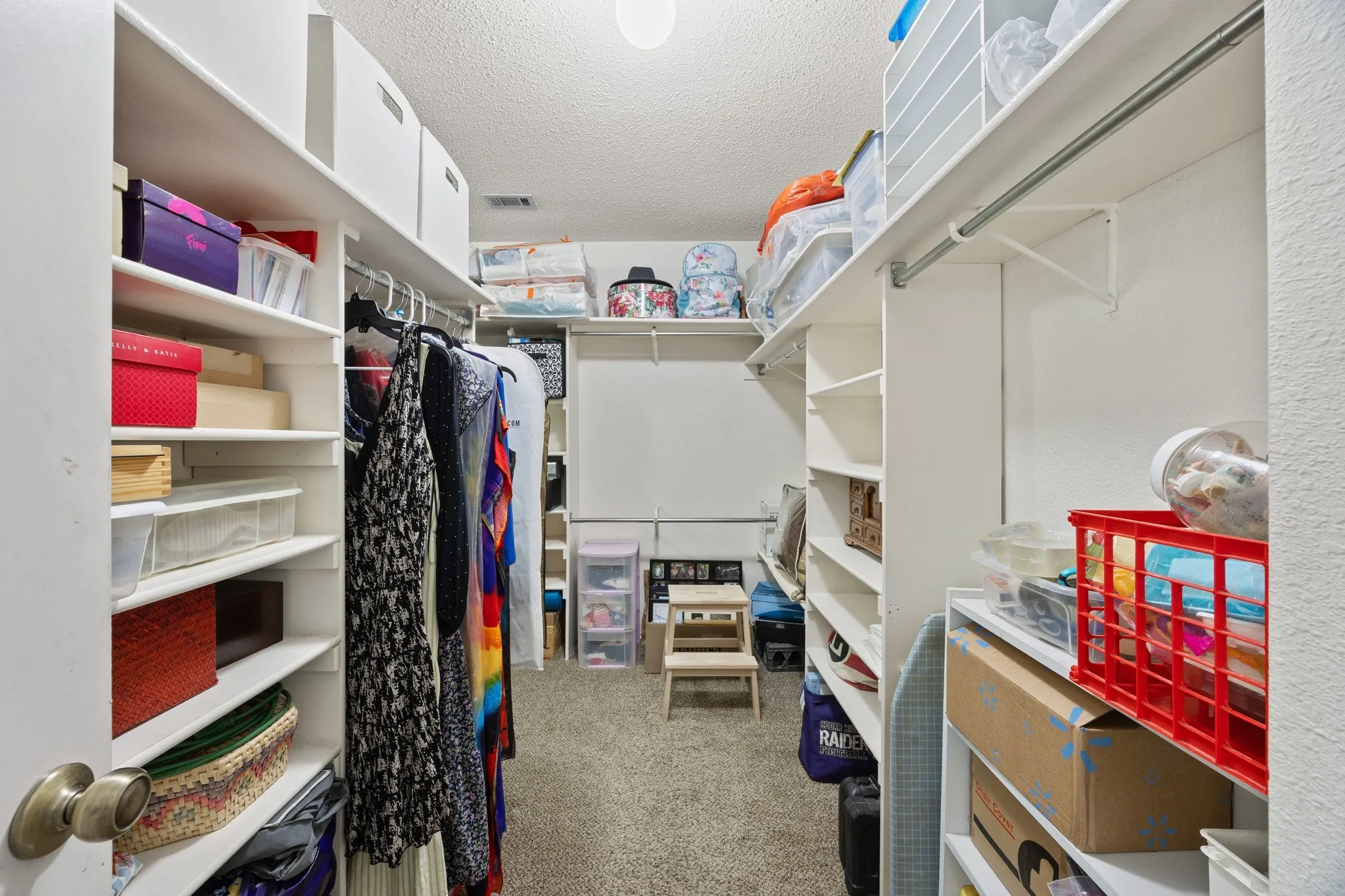 Walk-in closet with carpet flooring, white built-in shelving, and metal hanging rods