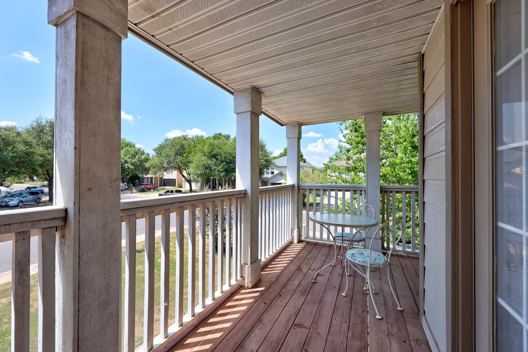 Expansive covered deck featuring composite decking, white aluminum railings, and substantial support columns, overlooking mature landscaping and tree-lined grounds
