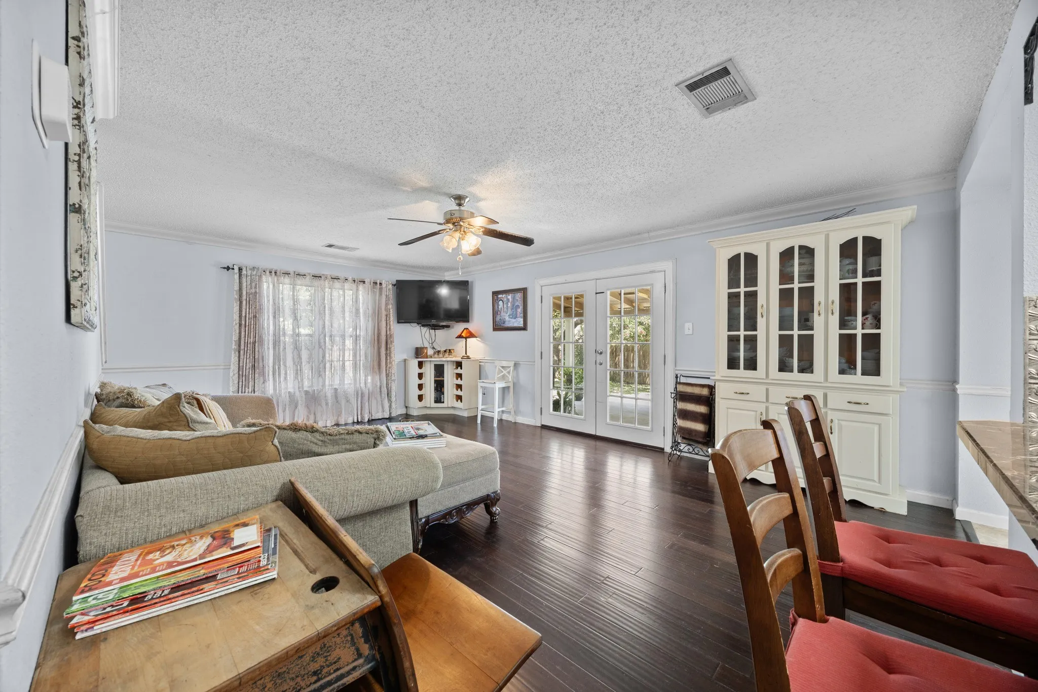 Dark wood-finish flooring throughout, ceiling fan with integrated lighting, built-in display cabinet with glass-front doors, and French patio doors with clear glass panes