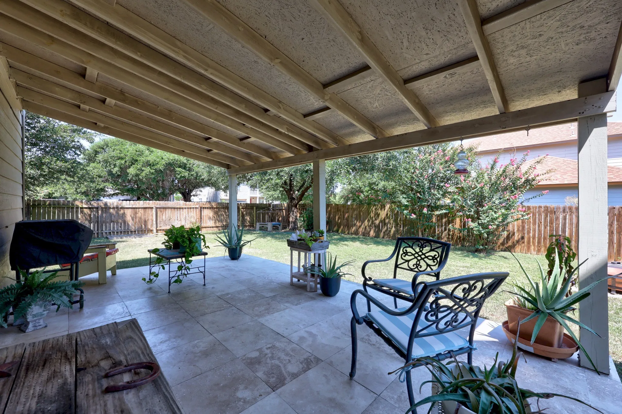 Expansive covered patio featuring a coffered ceiling with integrated soffit design, concrete flooring, and direct access to a manicured lawn bordered by mature landscaping