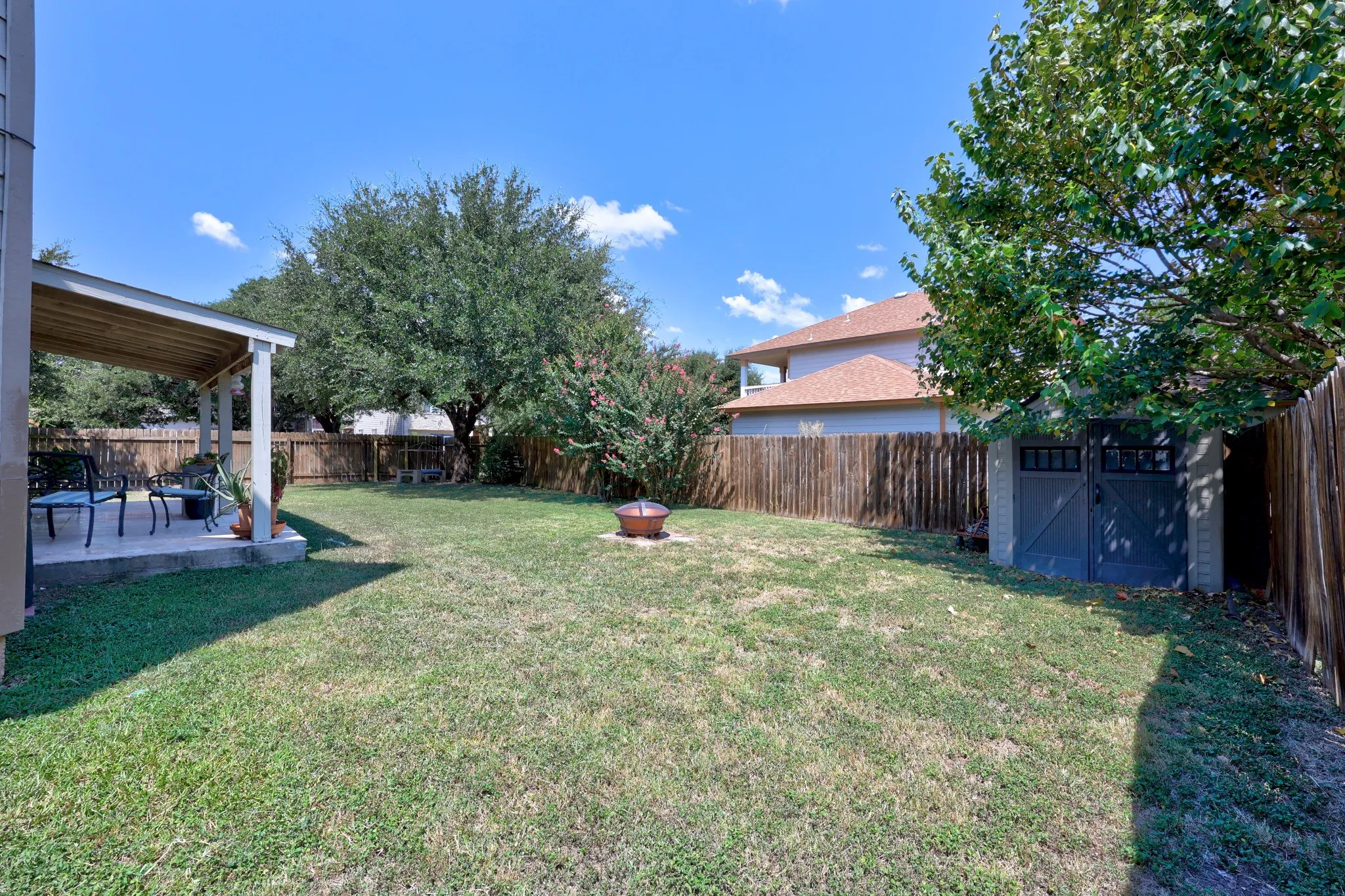 Expansive backyard featuring a covered patio, a privacy fence, and a storage shed