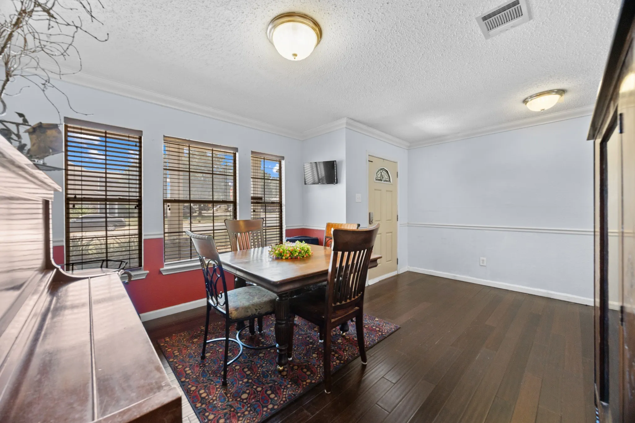 Bright dining area with dark wood-finish flooring, large multi-pane windows with plantation shutters, recessed ceiling lighting, and access to an outdoor patio