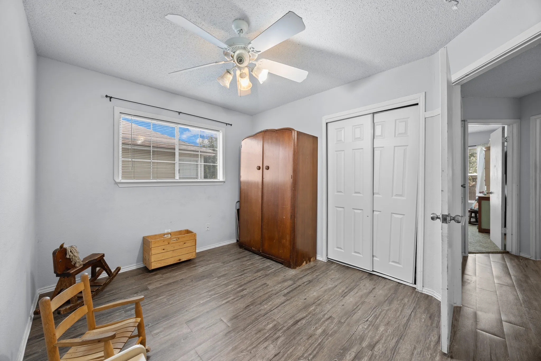 Wood-finish flooring, ceiling fan with integrated lighting, window with white trim, and a bi-fold closet