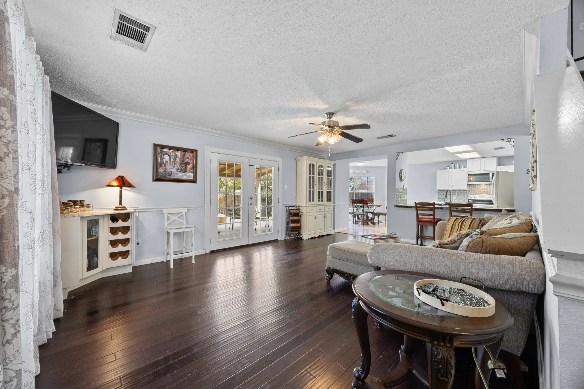 Wood-finish flooring, built-in cabinetry, crown molding, double French doors, and ceiling fan
