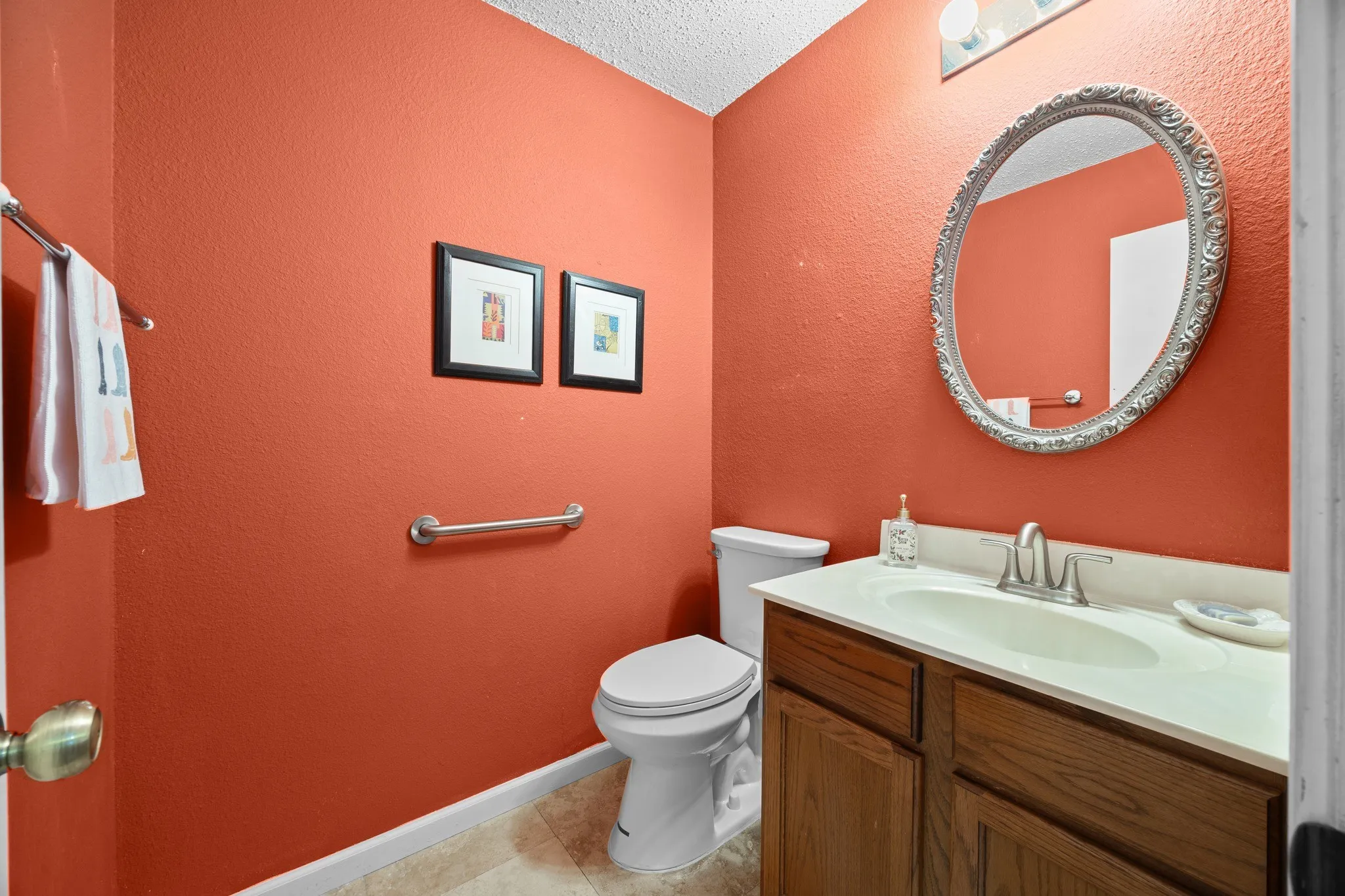 Vibrant coral walls create a warm, inviting powder room featuring a wood-finish vanity with dual drawers, white countertop, and chrome faucet