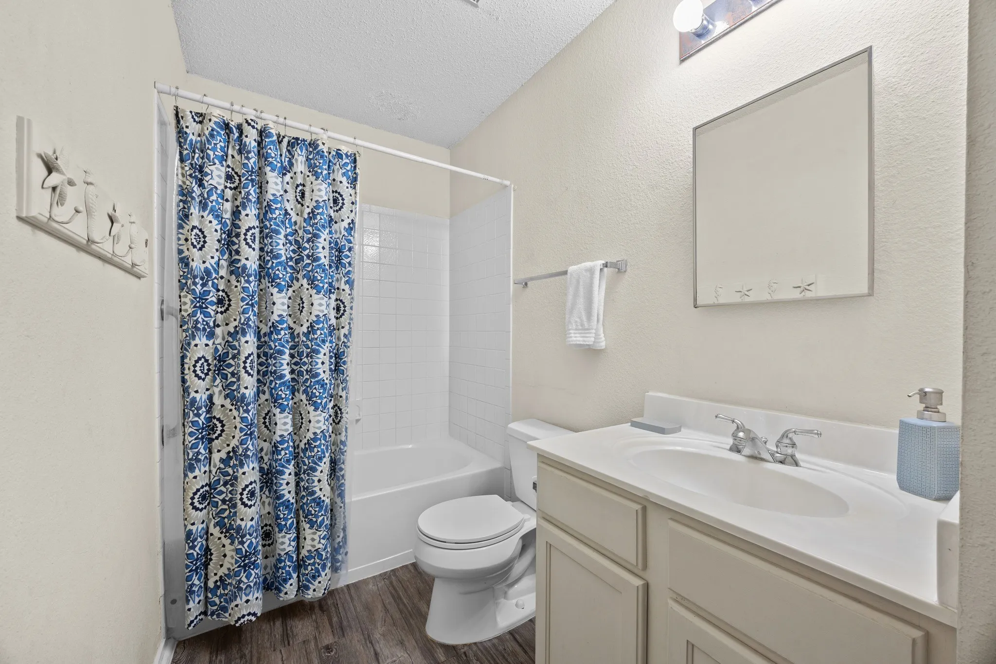 Spa-inspired bathroom featuring a dual-sink vanity with ample storage, white subway tile surround, wood-finish flooring, and a blue geometric tile shower curtain