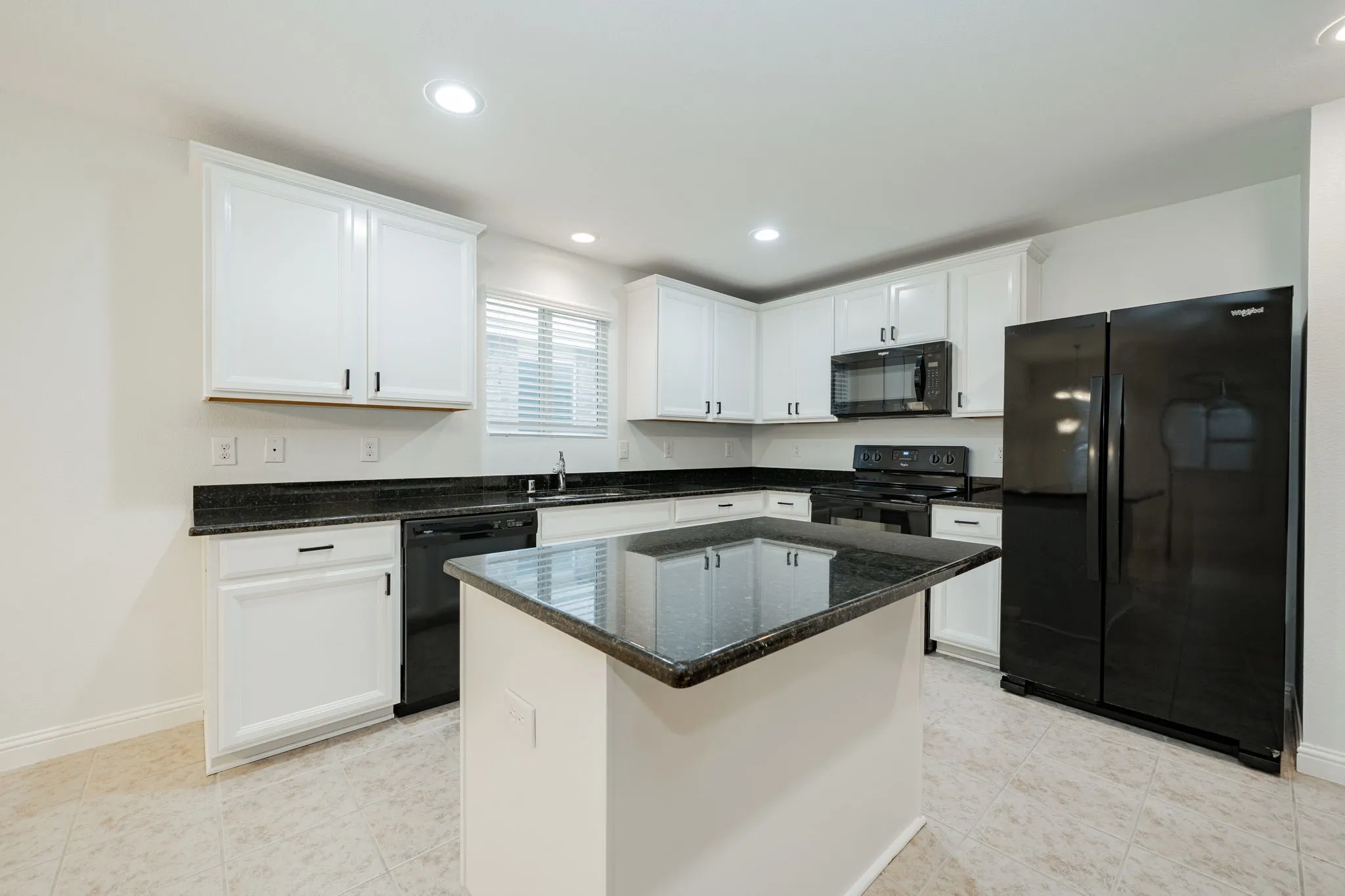 Kitchen featuring black appliances, white cabinets, dark stone countertops, recessed lighting, and a center island