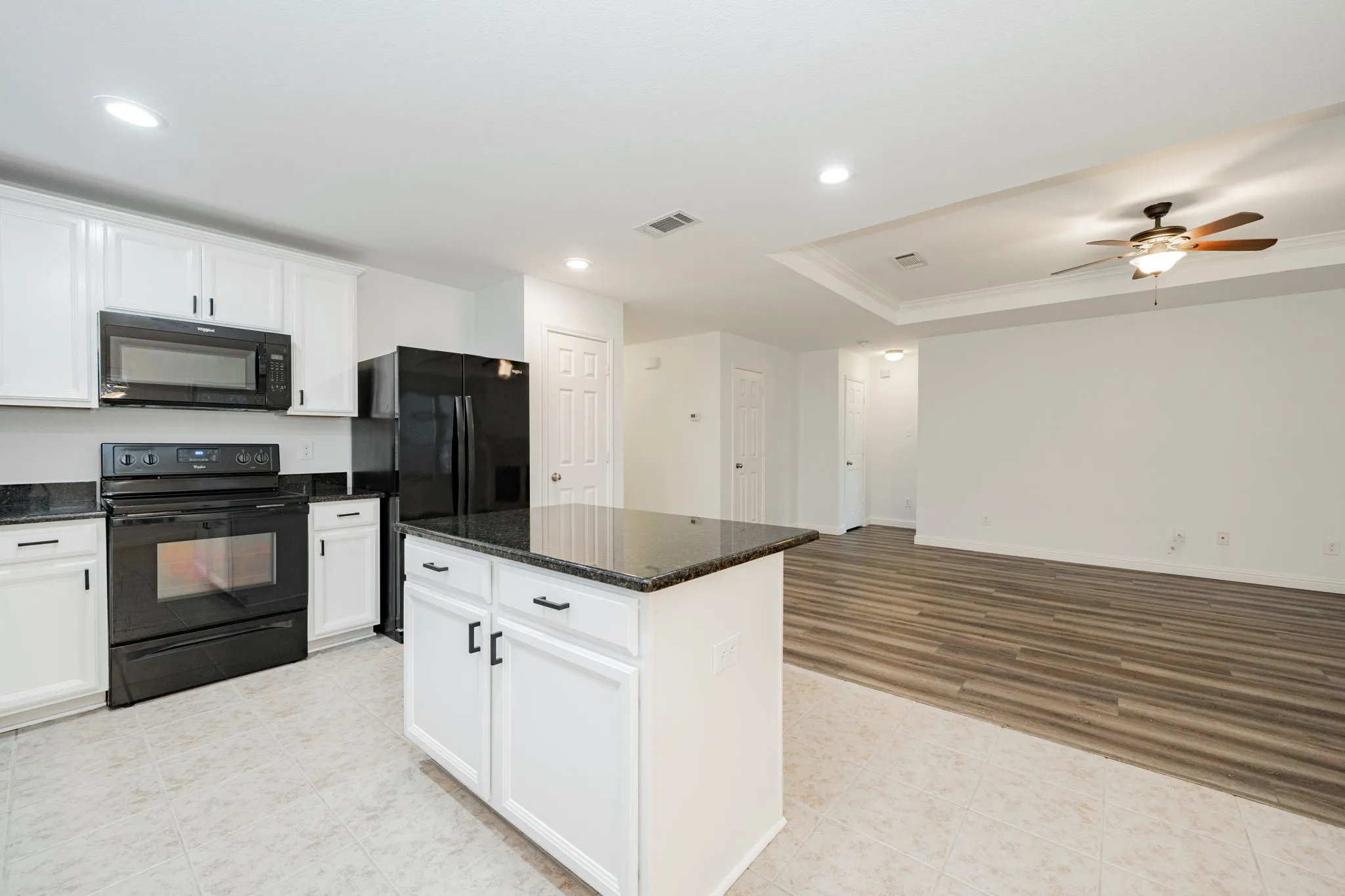 Kitchen featuring black appliances, ornamental molding, white cabinets, ceiling fan, and a raised ceiling