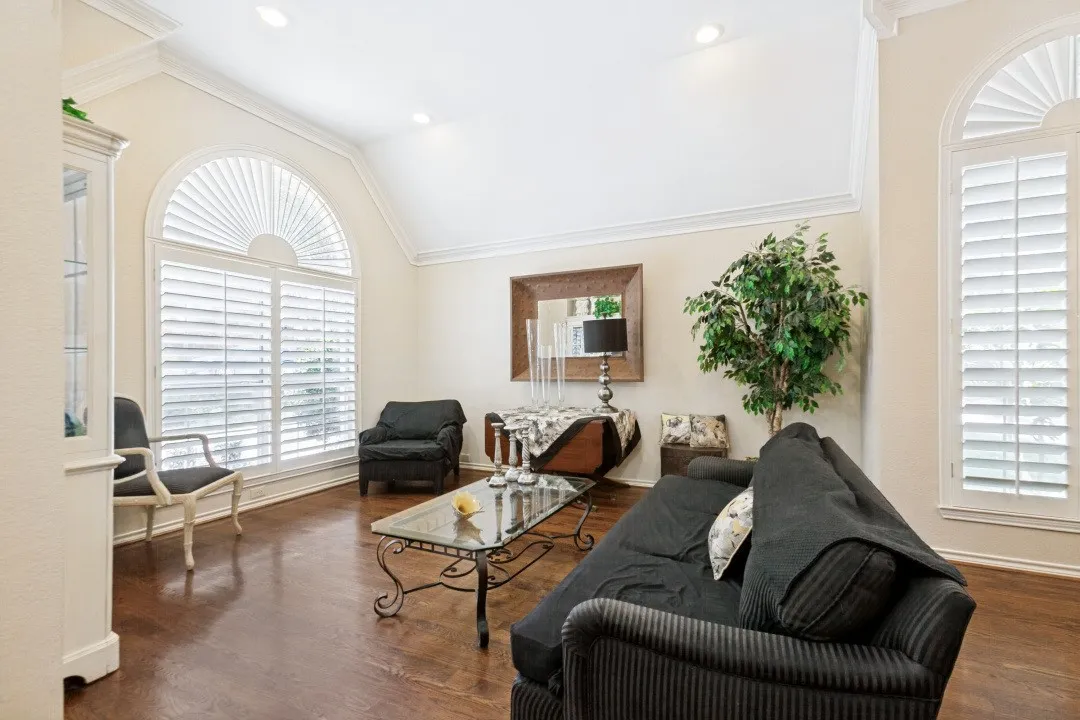 Hardwood flooring, arched windows with plantation shutters, vaulted ceiling, recessed lighting, and crown molding