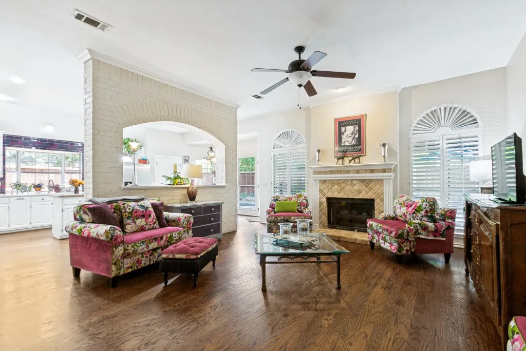 Hardwood flooring, arched brick wall opening, fireplace with tile surround, white cabinetry, and plantation shutters