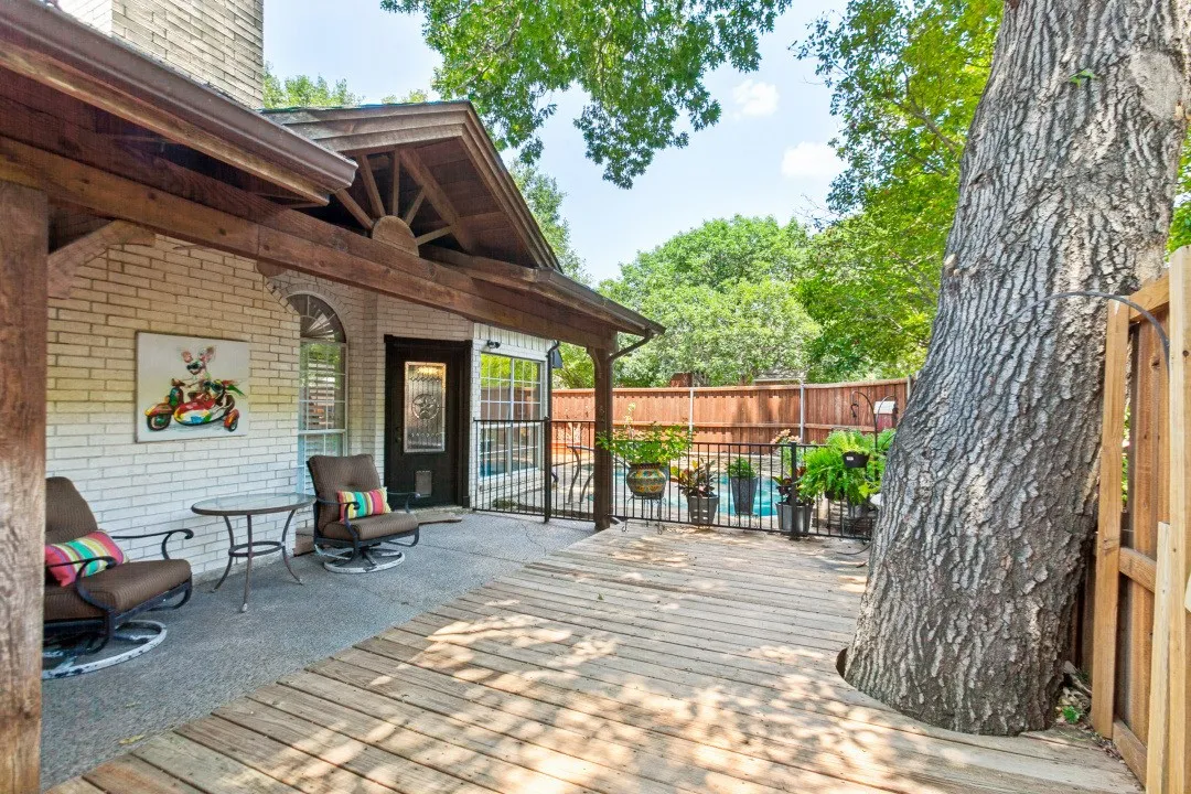Expansive wood deck with a large mature tree integration, leading to a concrete patio