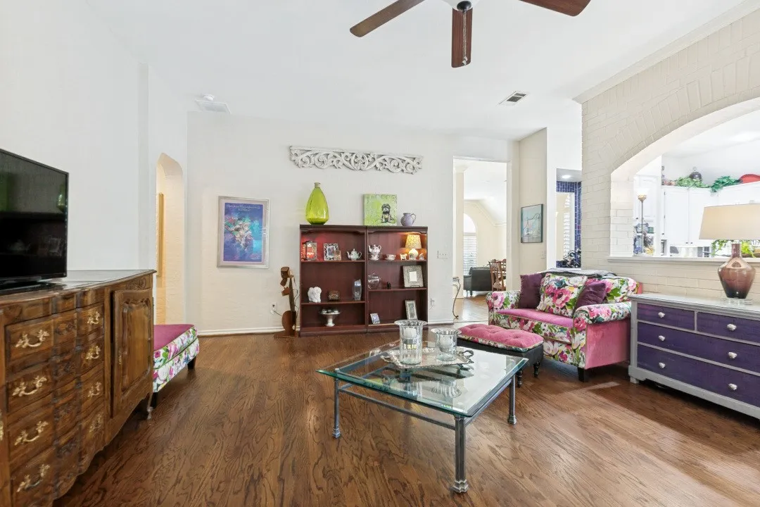 Hardwood flooring throughout, a ceiling fan, and an arched brick-finish passthrough