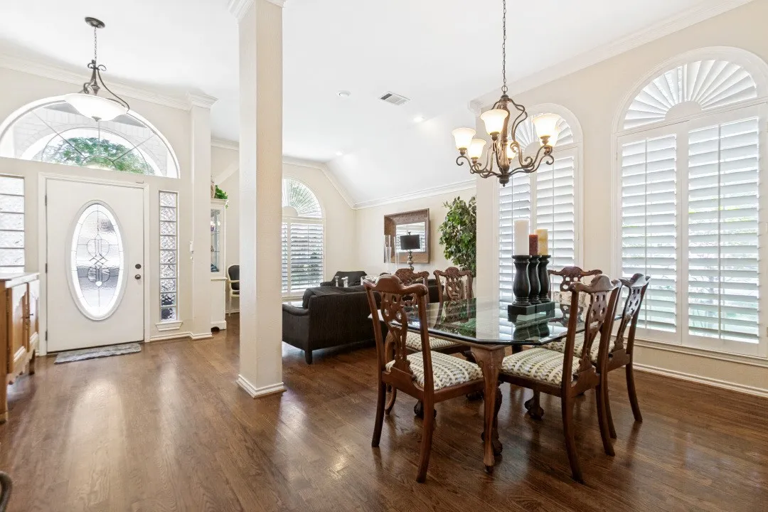 Wood-finish flooring, arched windows with plantation shutters, decorative glass front door with transom, and chandelier lighting