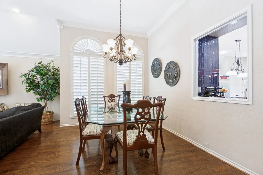 Hardwood flooring, arched windows with plantation shutters, vaulted ceiling, crown molding, and a built-in kitchen pass-through