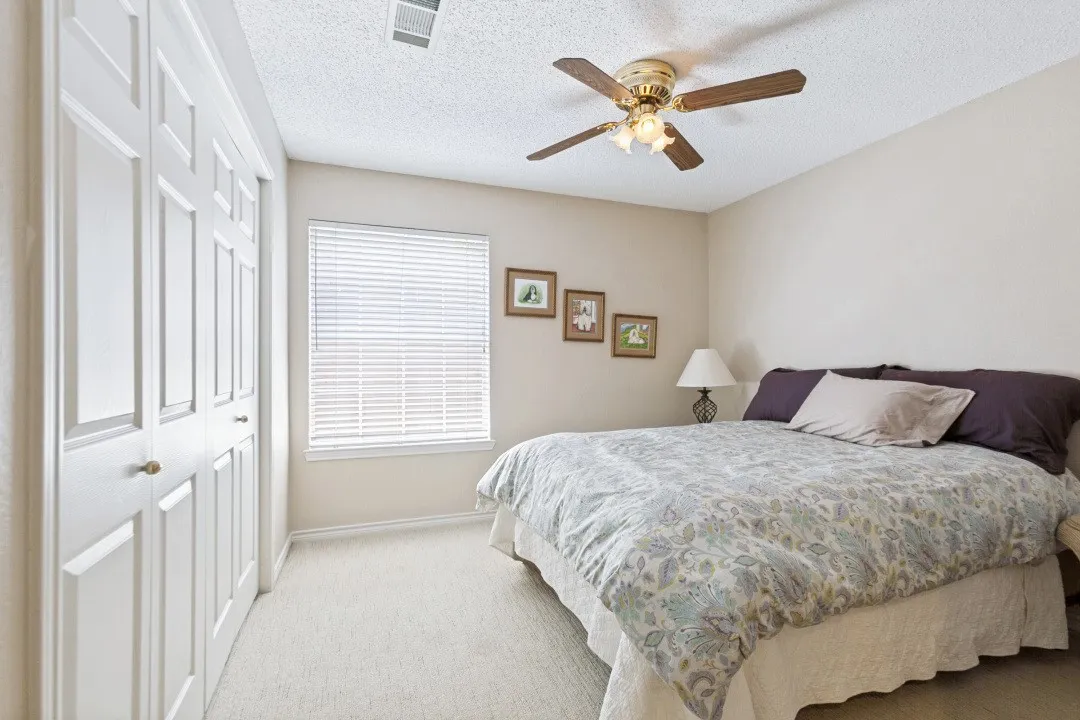 Carpeted room featuring white bi-fold closet doors, a window with horizontal blinds, a ceiling fan with integrated lighting, and neutral wall tones