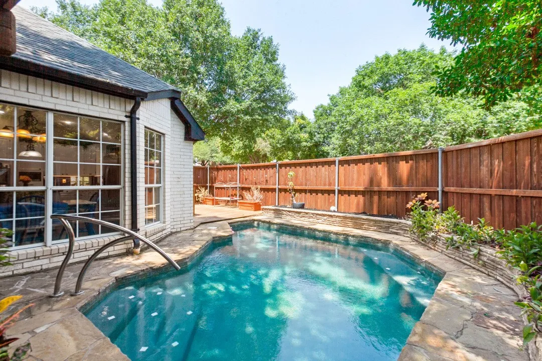 Backyard with a shaped swimming pool, stone coping, wood privacy fence, and mature perimeter trees