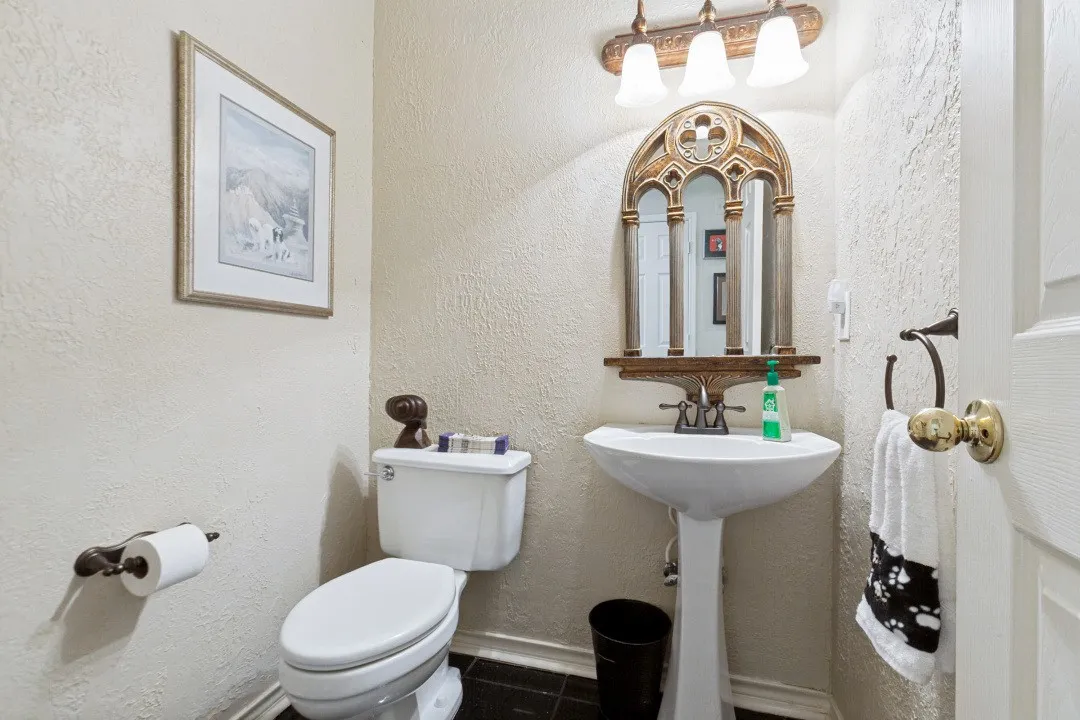 Pedestal sink, wall-mounted light fixture, decorative mirror, and dark-toned flooring