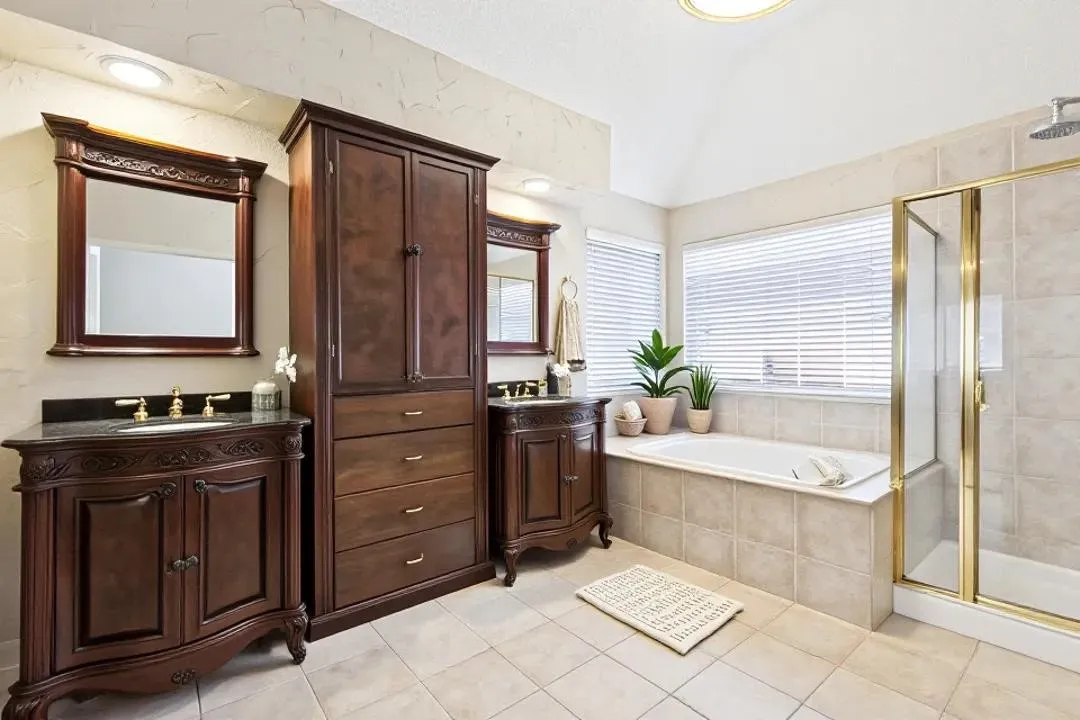 Dual wood-finish vanities with dark countertops, built-in soaking tub, separate glass-enclosed shower, and tile flooring