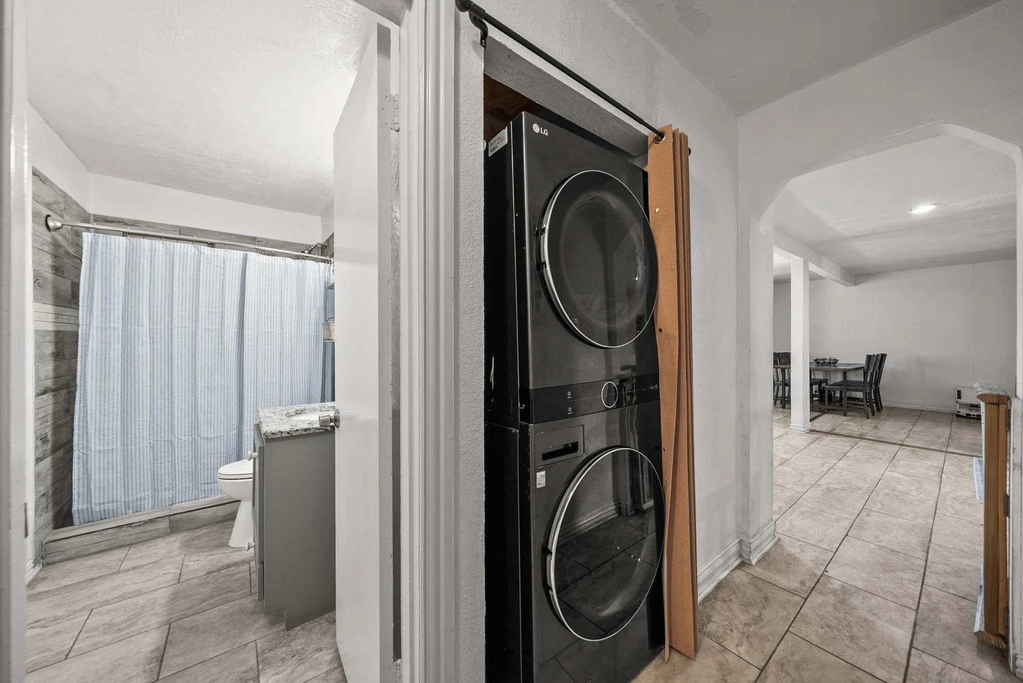Stacked laundry appliances, tiled flooring, arched doorway, and built-in vanity with countertop