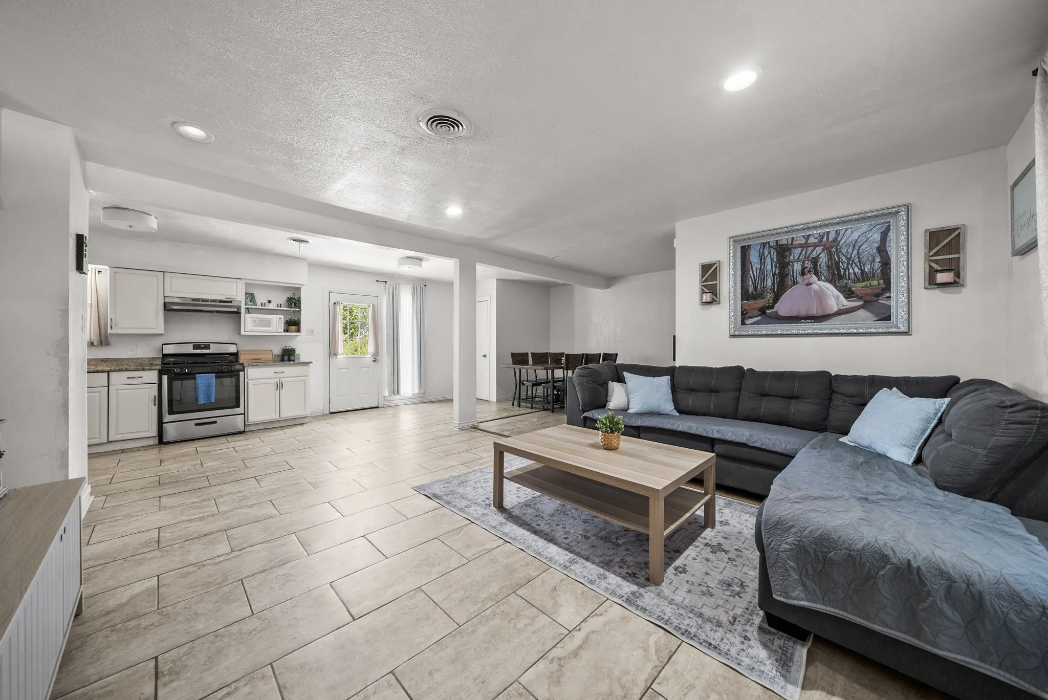 Open-concept living space featuring recessed lighting, tile flooring, and a kitchen with white cabinetry, stainless steel appliances, and a granite-style countertop