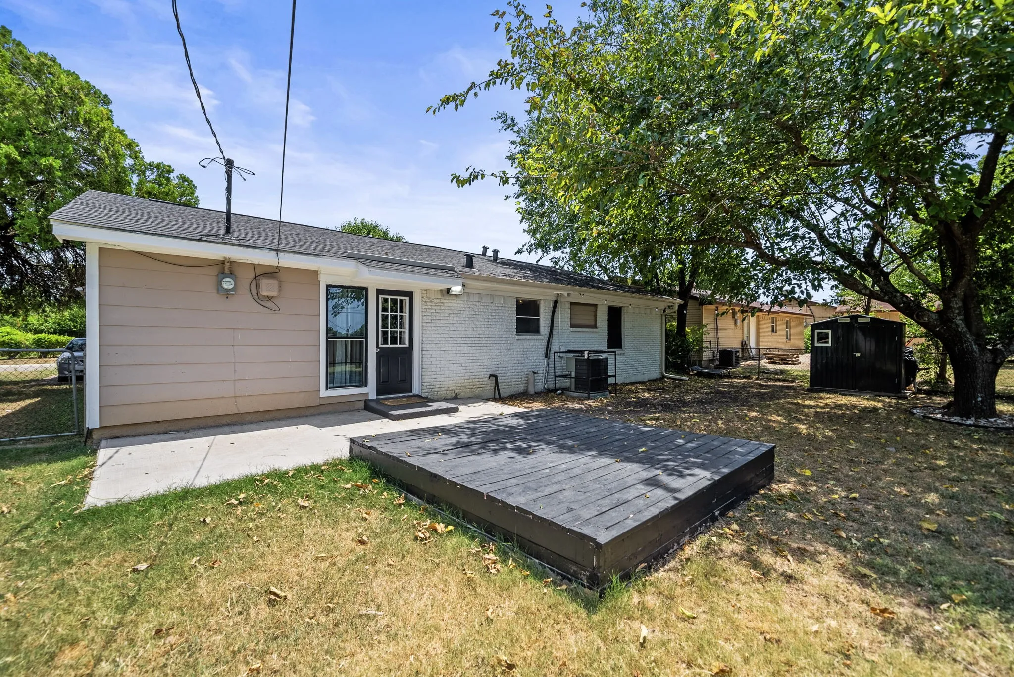 Backyard featuring a ground-level deck, concrete patio, mature trees, and a utility shed