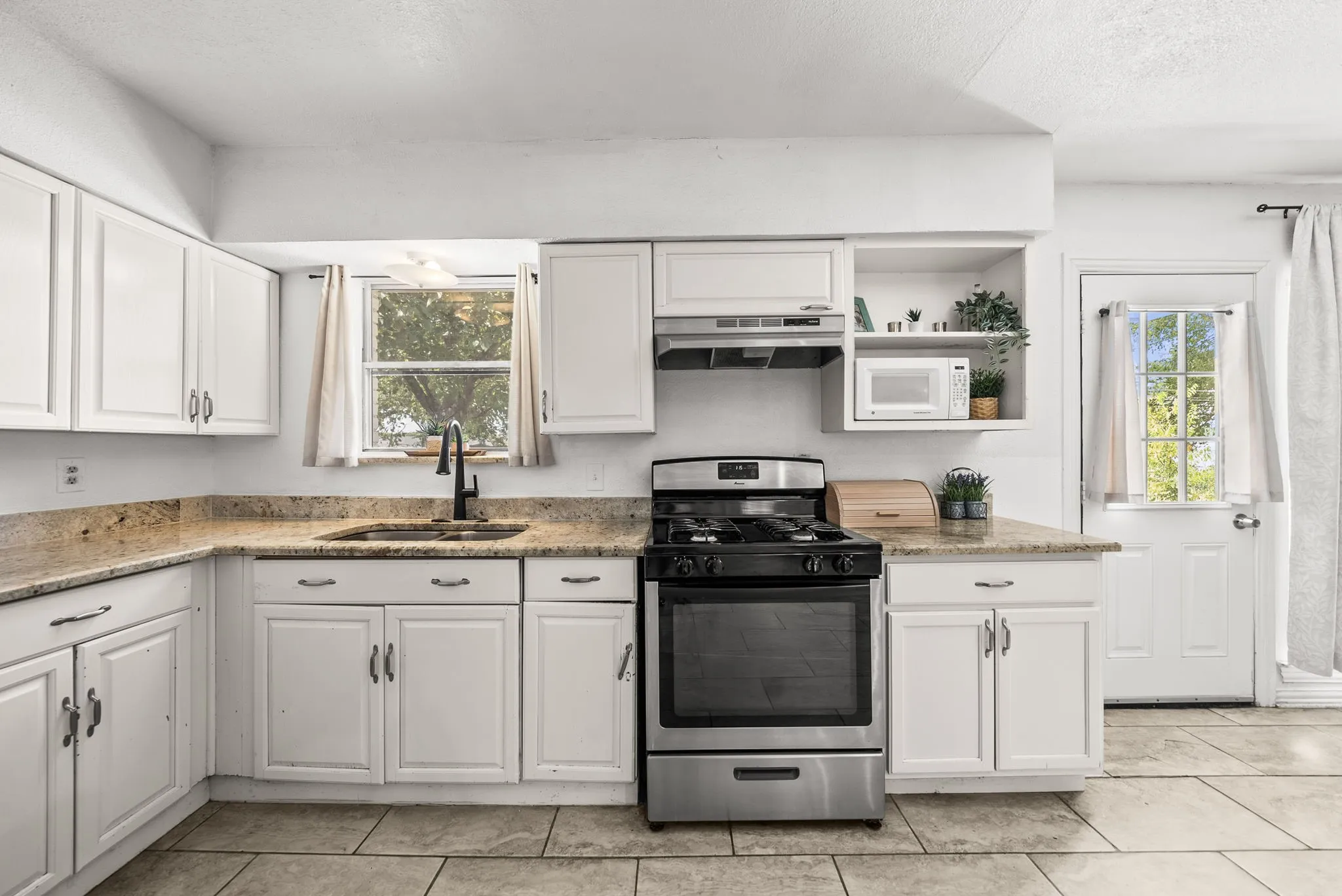White cabinetry, granite-finish countertops, stainless steel range with overhead ventilation, and tile flooring