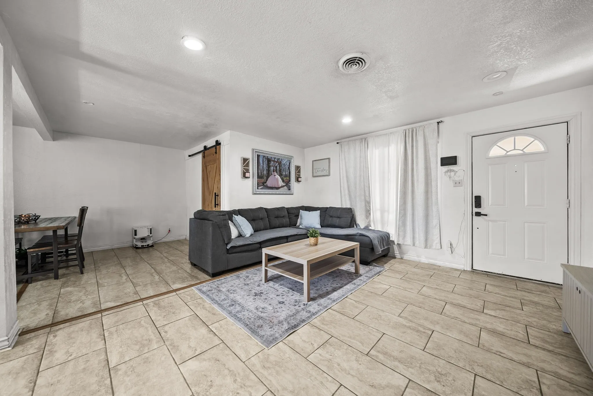Recessed lighting, wood-look tile flooring, white entry door with frosted glass insert, and a wood-finish barn door