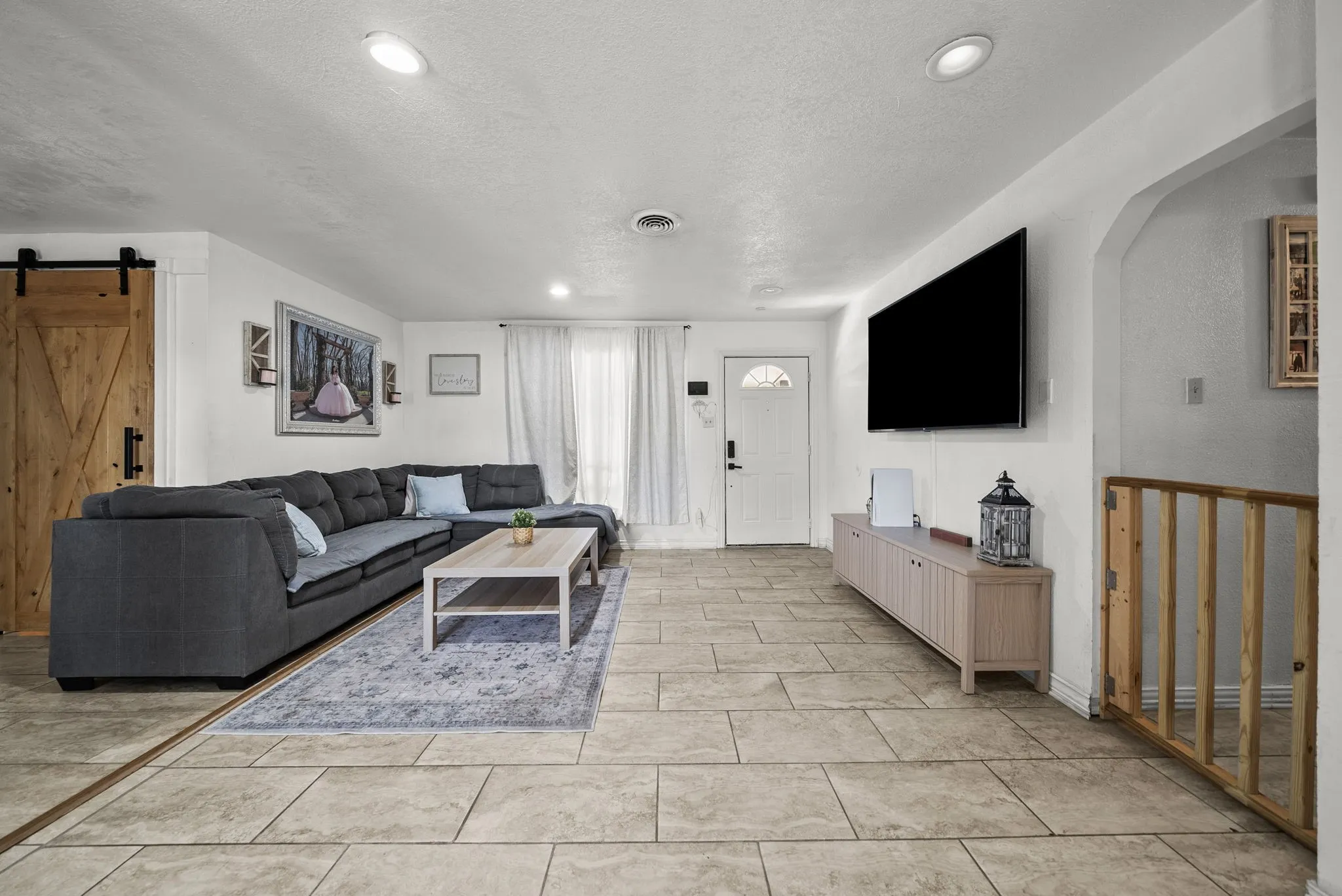 Recessed lighting, wood-finish barn door, arched doorway, tile flooring, and a window with curtains