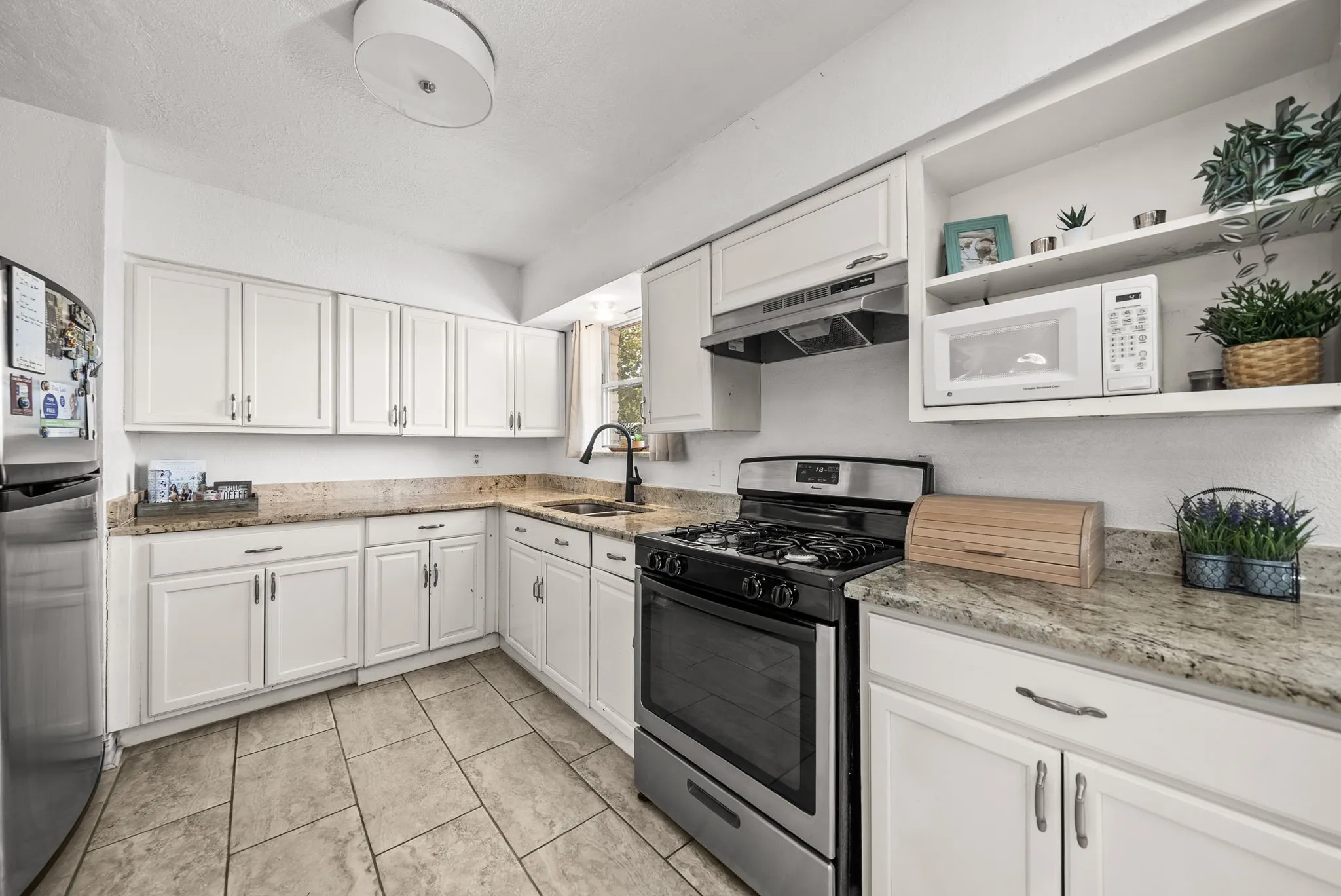 Kitchen featuring white cabinetry, light-toned countertops, a stainless steel gas range, a stainless steel refrigerator, and tiled flooring
