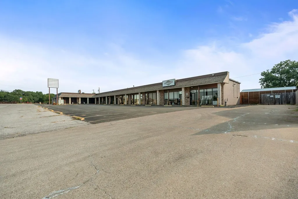 Single-story commercial building with multiple storefronts, extensive paved parking area, and a prominent freestanding sign structure