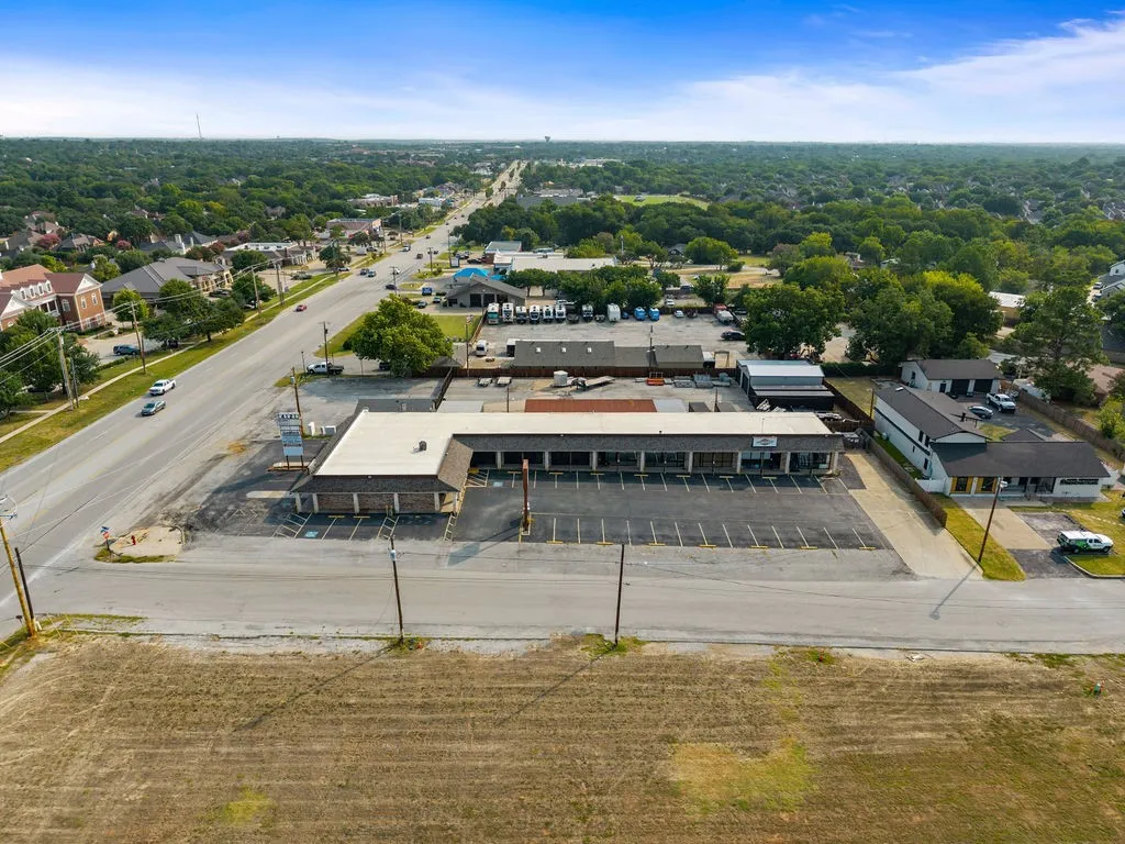Commercial property featuring a multi-unit building with a large parking area, situated along a paved roadway